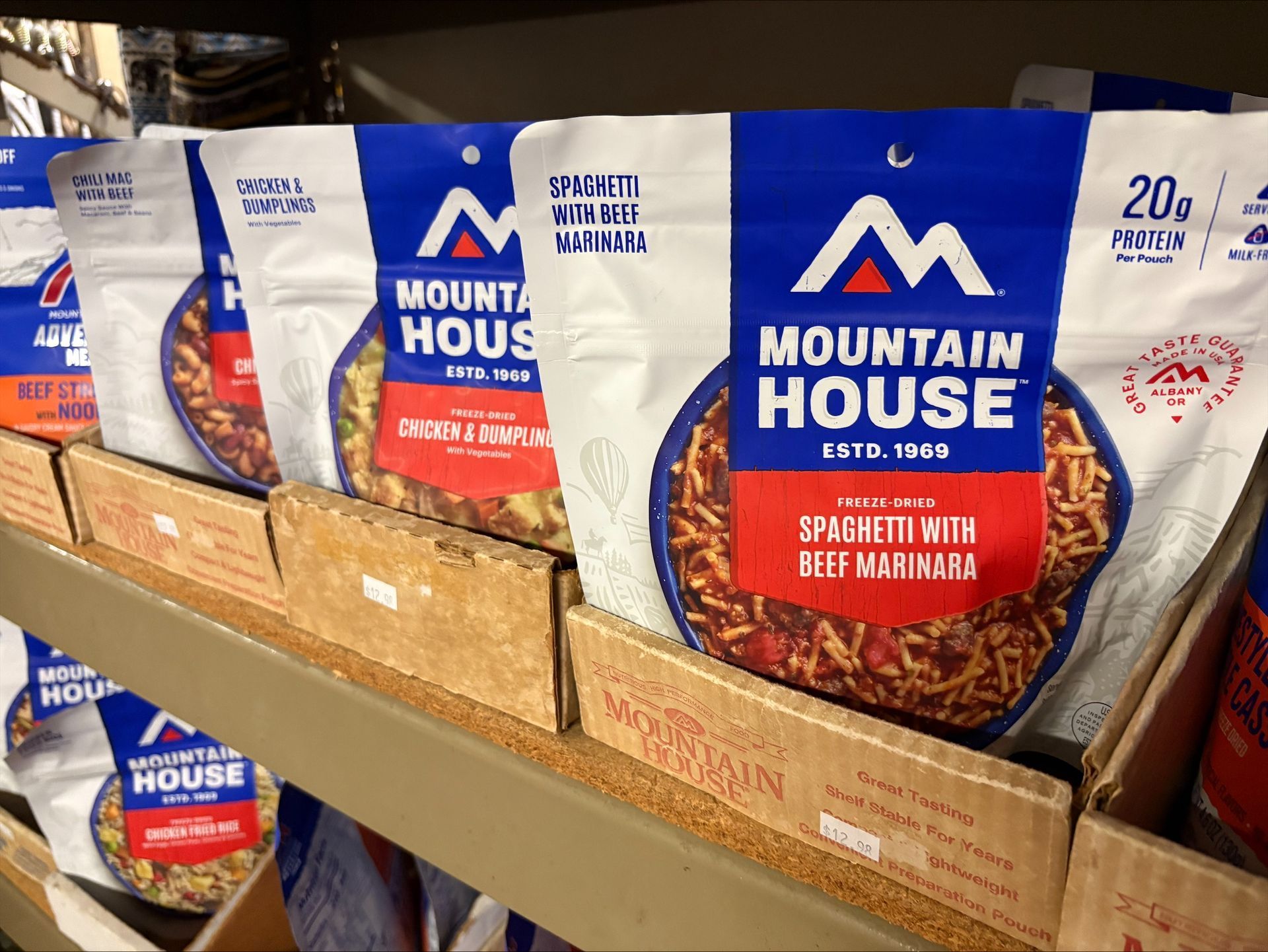 Shelf of Mountain House freeze-dried food pouches, various flavors with blue and white packaging.