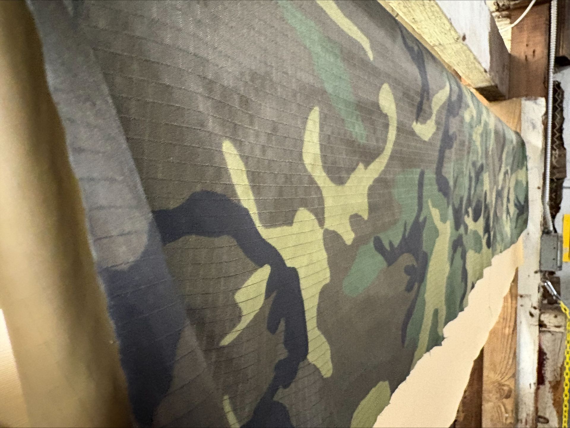 Camouflage fabric tacked to a wooden beam in a building.