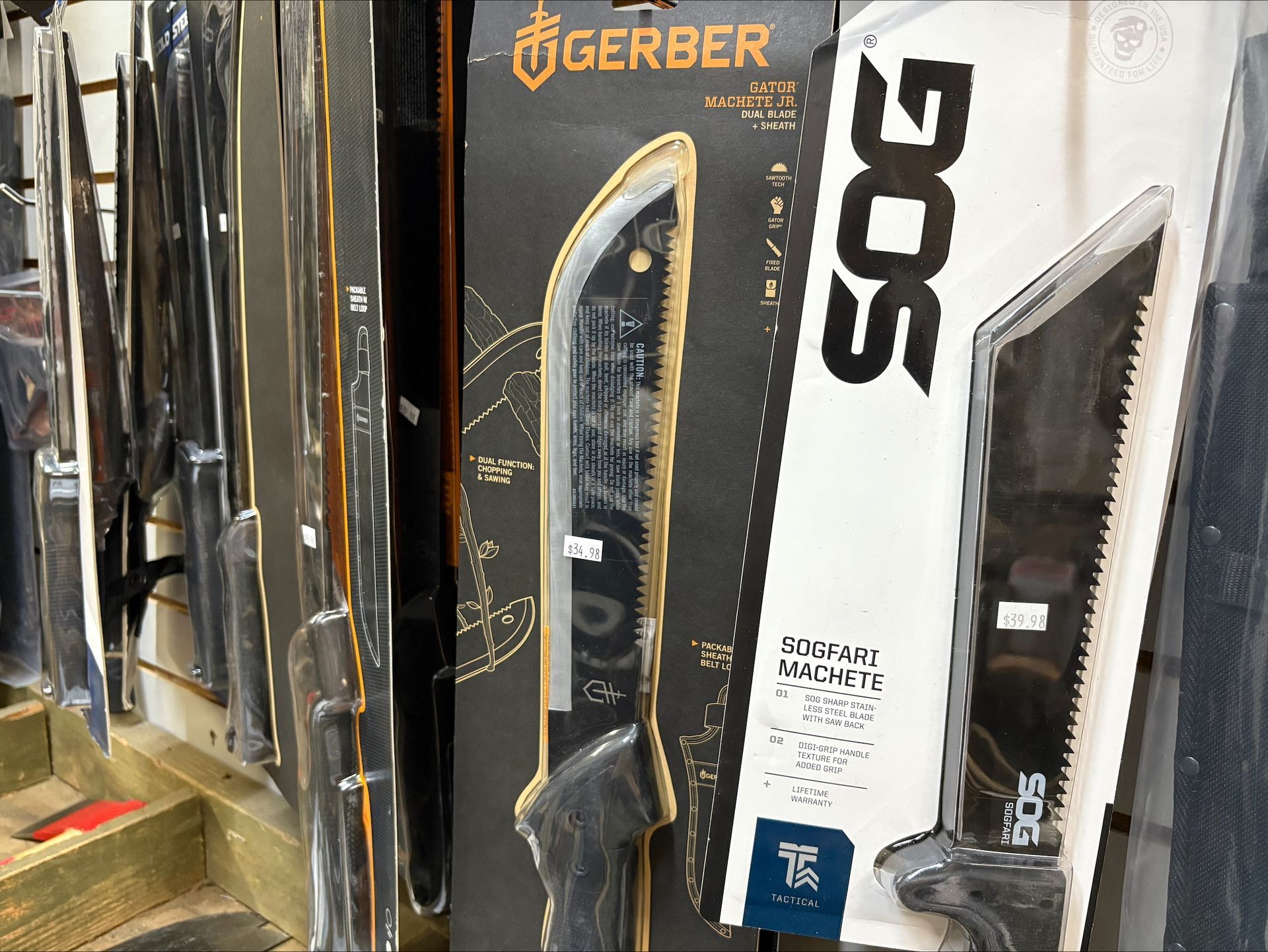 Knives and machetes in packaging displayed on a retail shelf, including Gerber and SOG brands.