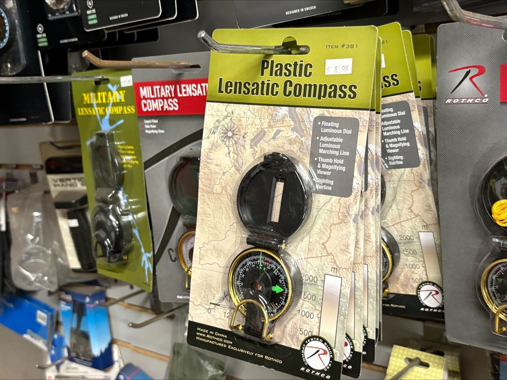 Row of packaged plastic lensatic compasses for sale, on a retail shelf.