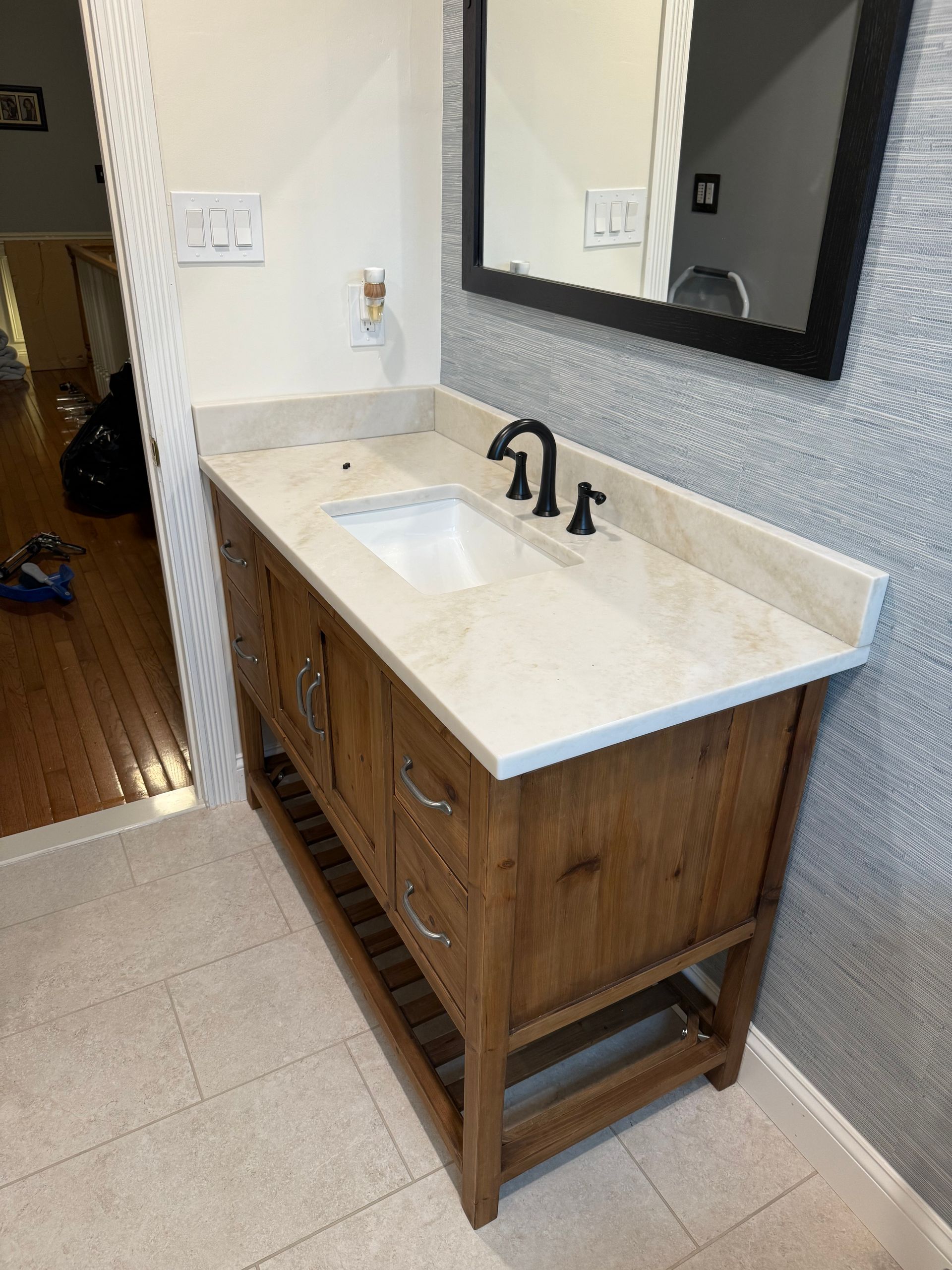 Bathroom vanity with wood cabinet, light countertop, white sink, black faucet, and large mirror.