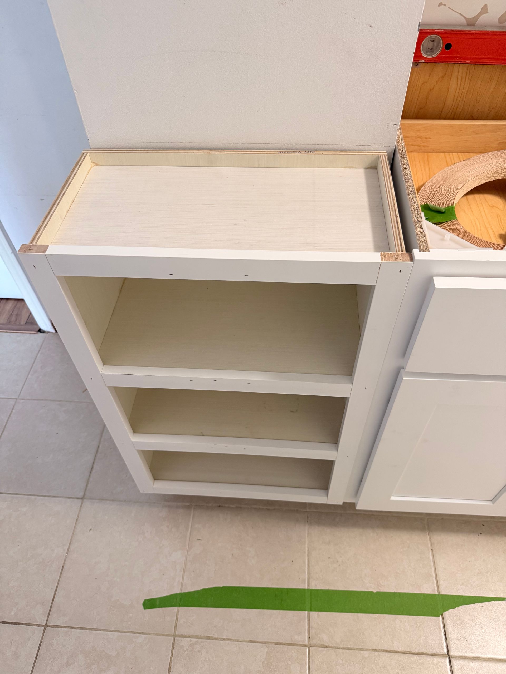 White kitchen cabinet with three shelves, adjacent to another cabinet and a countertop with visible construction.