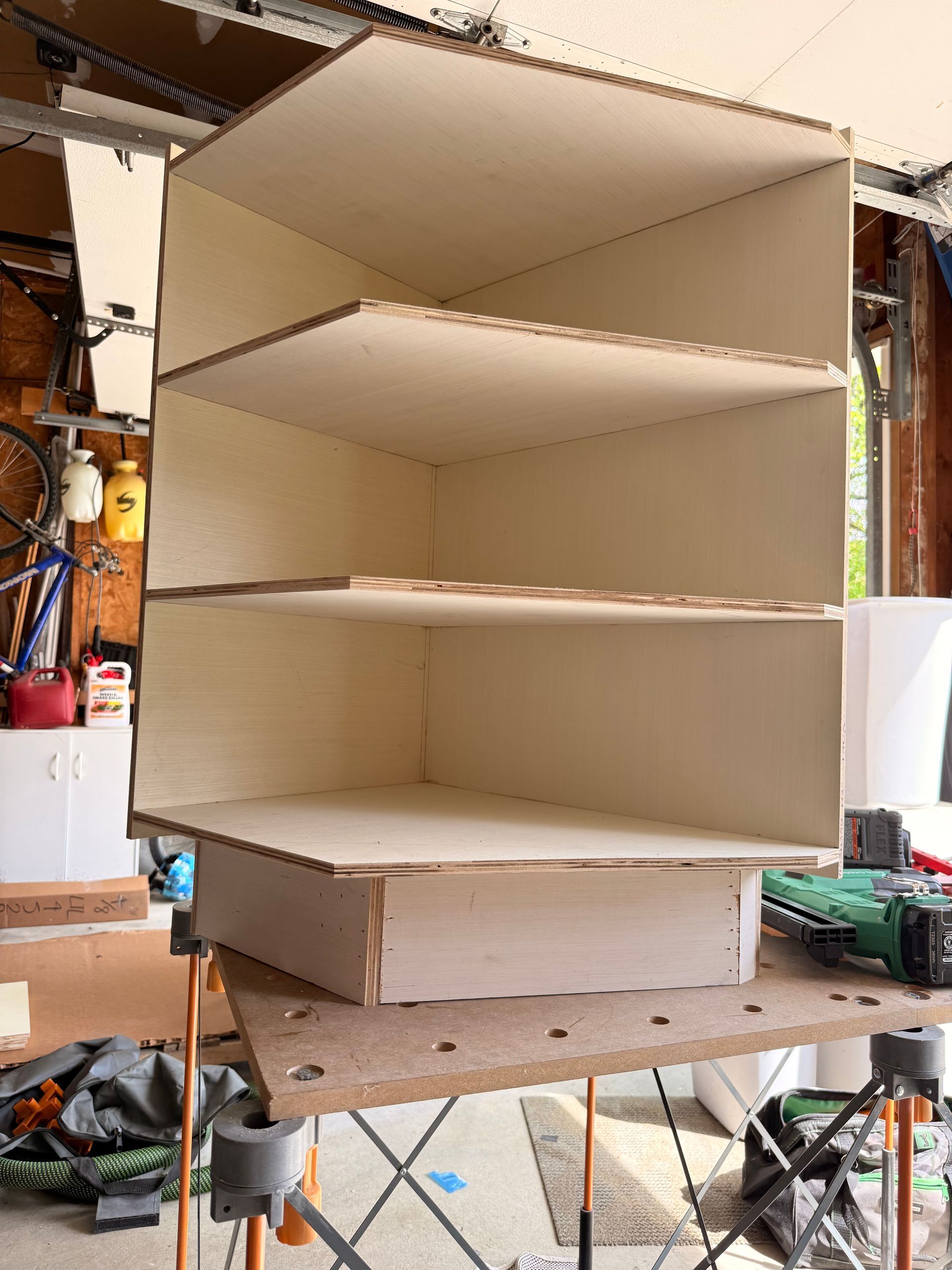 Wooden shelving unit under construction in a garage, with three shelves.