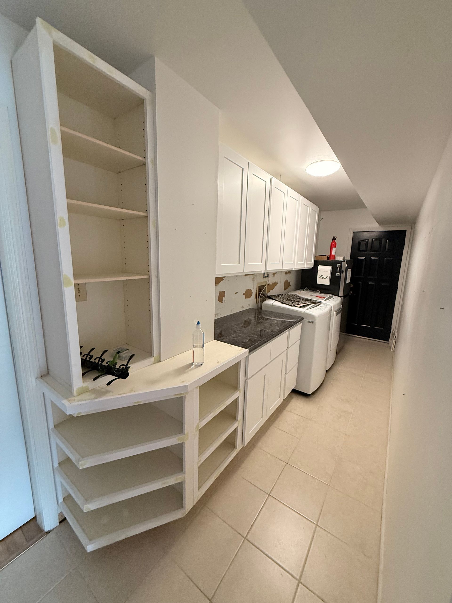 White kitchen with cabinets, stove, and open shelving, in a narrow room with tile flooring.