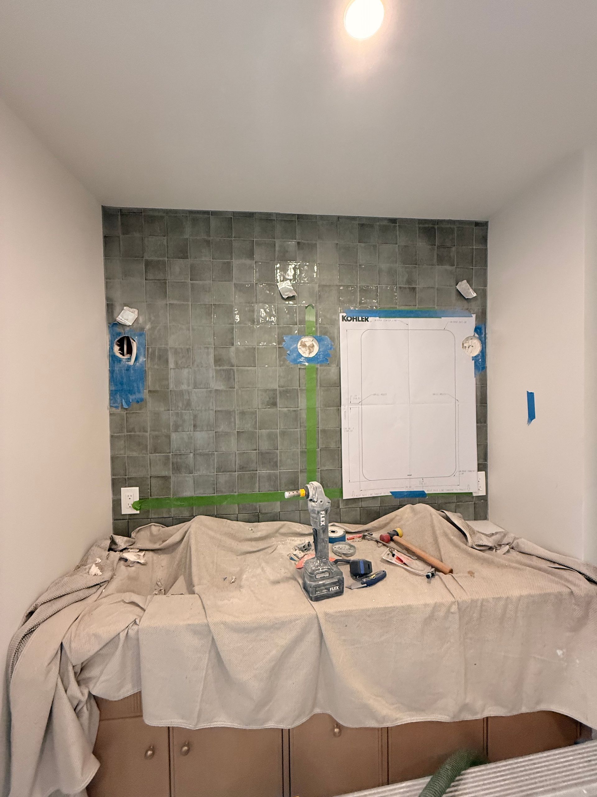 Bathroom renovation in progress; tile backsplash, covered countertop, tools, cabinets, and a blueprint are visible.
