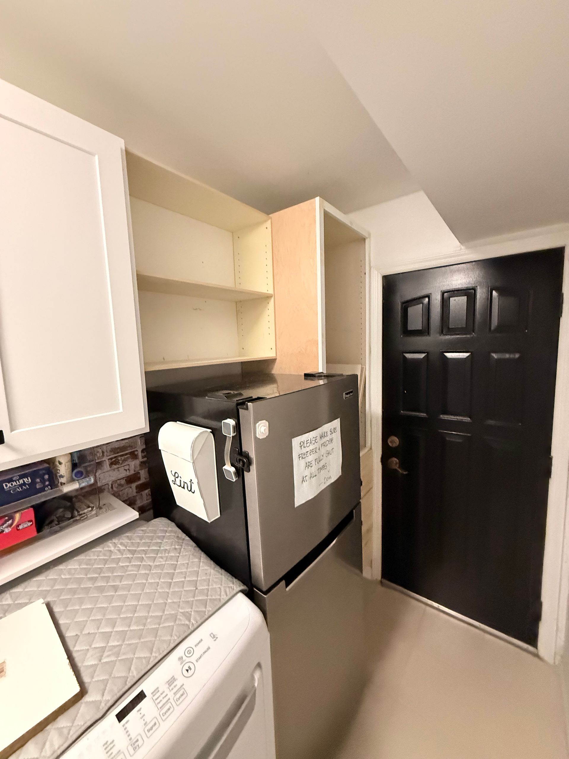 Refrigerator in a kitchen alcove next to a black door and white cabinets.