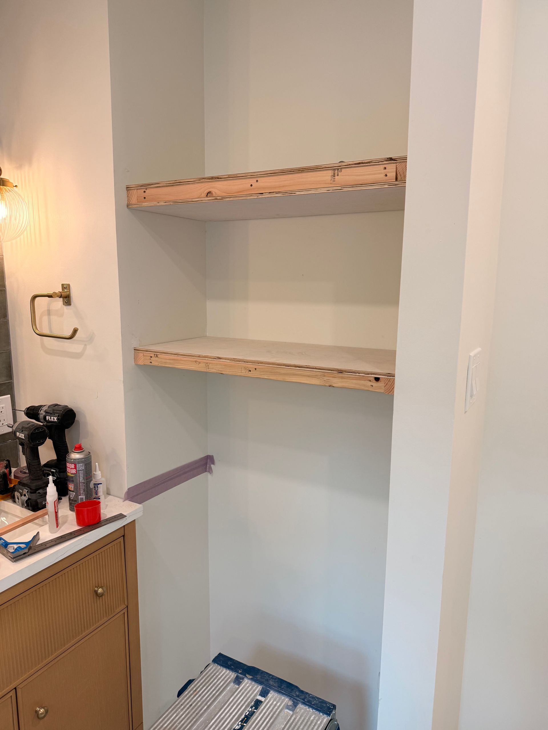Built-in bathroom shelves, white walls, two shelves, light wood edging, tape on wall.