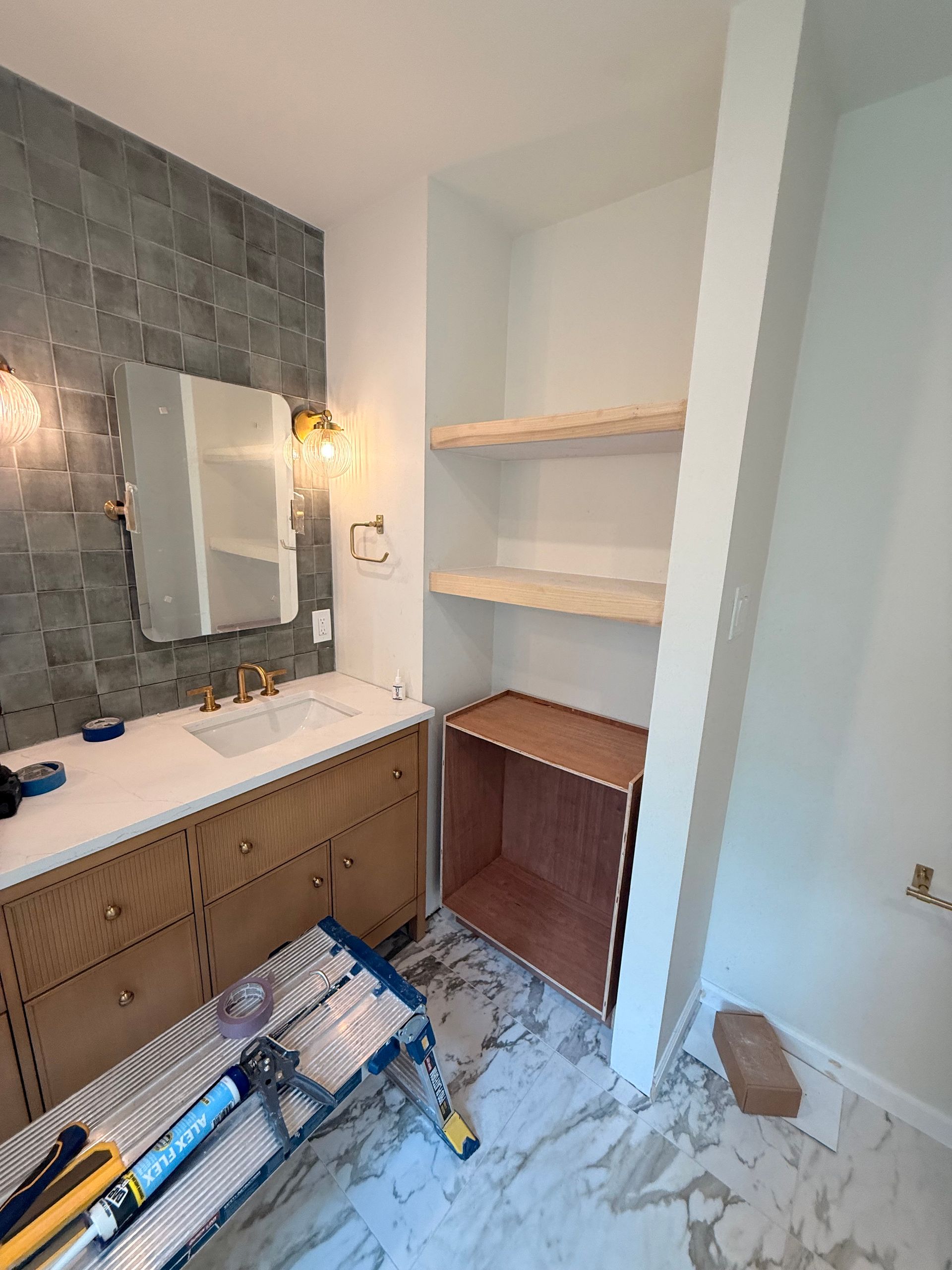 Bathroom with light wood vanity, shelves, marble floors, and gray tile backsplash.