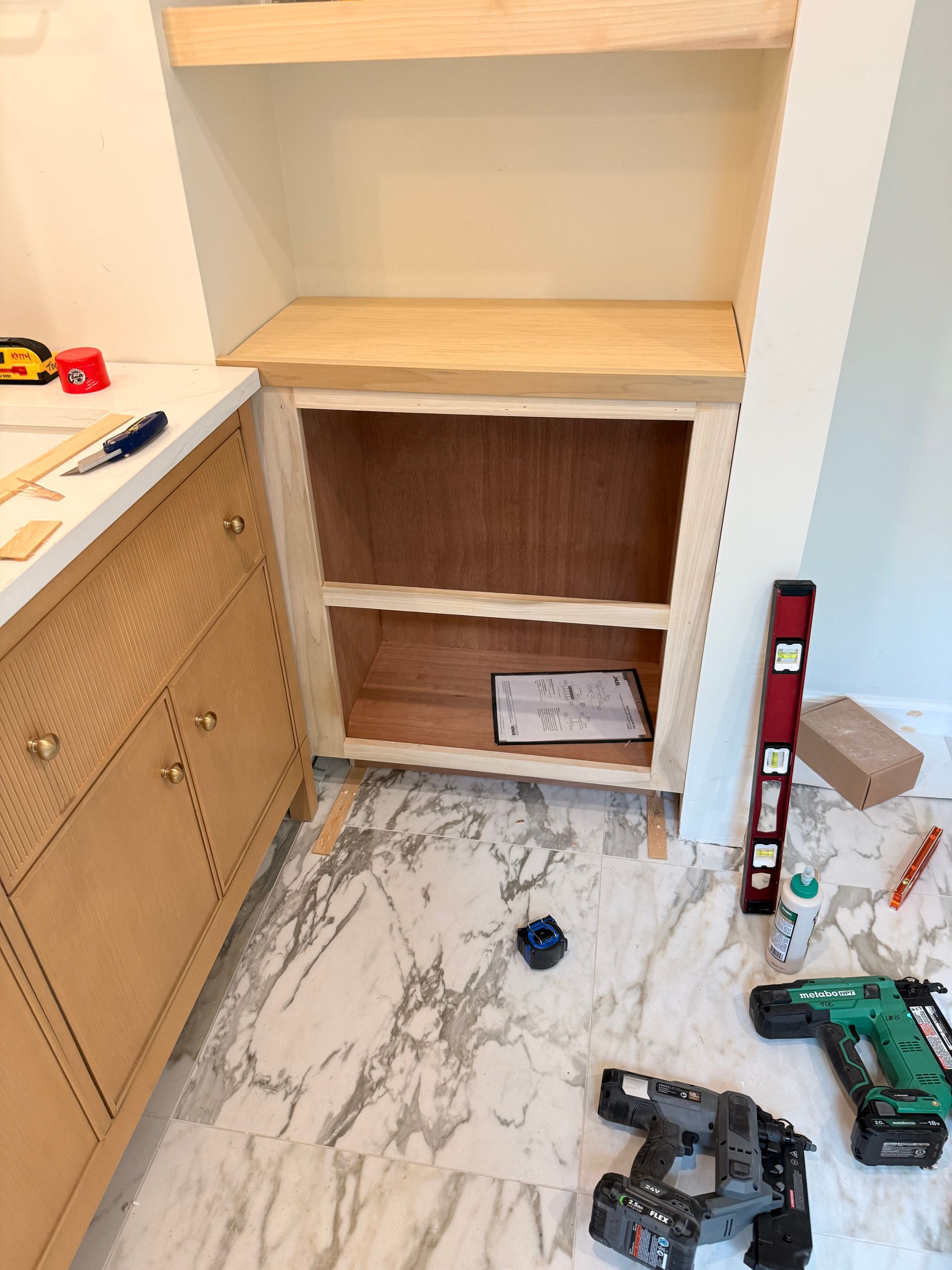 Built-in cabinet under construction with tools on the floor and adjacent countertop.