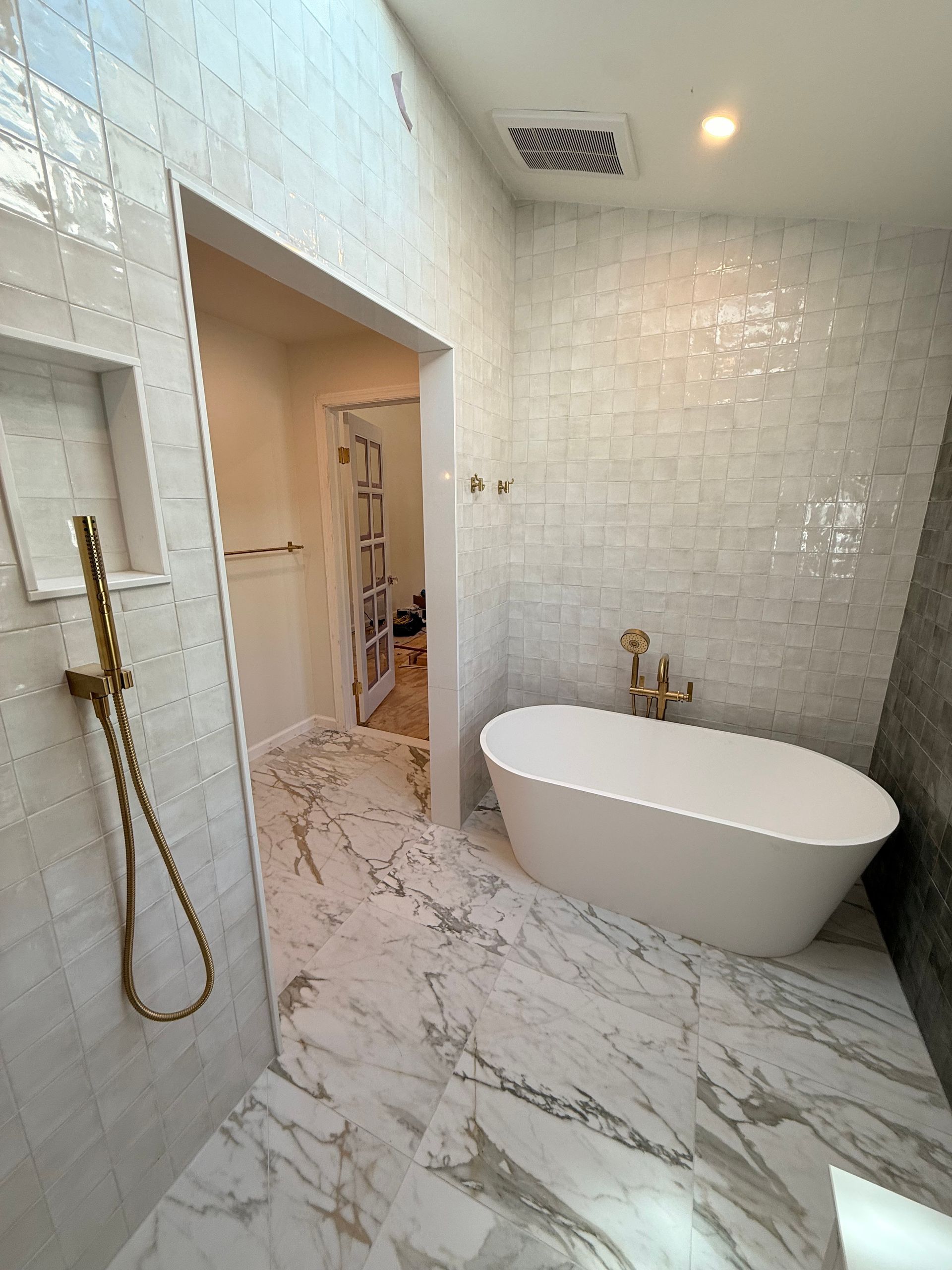 Luxurious white bathroom with a freestanding tub, gold fixtures, and marble flooring.