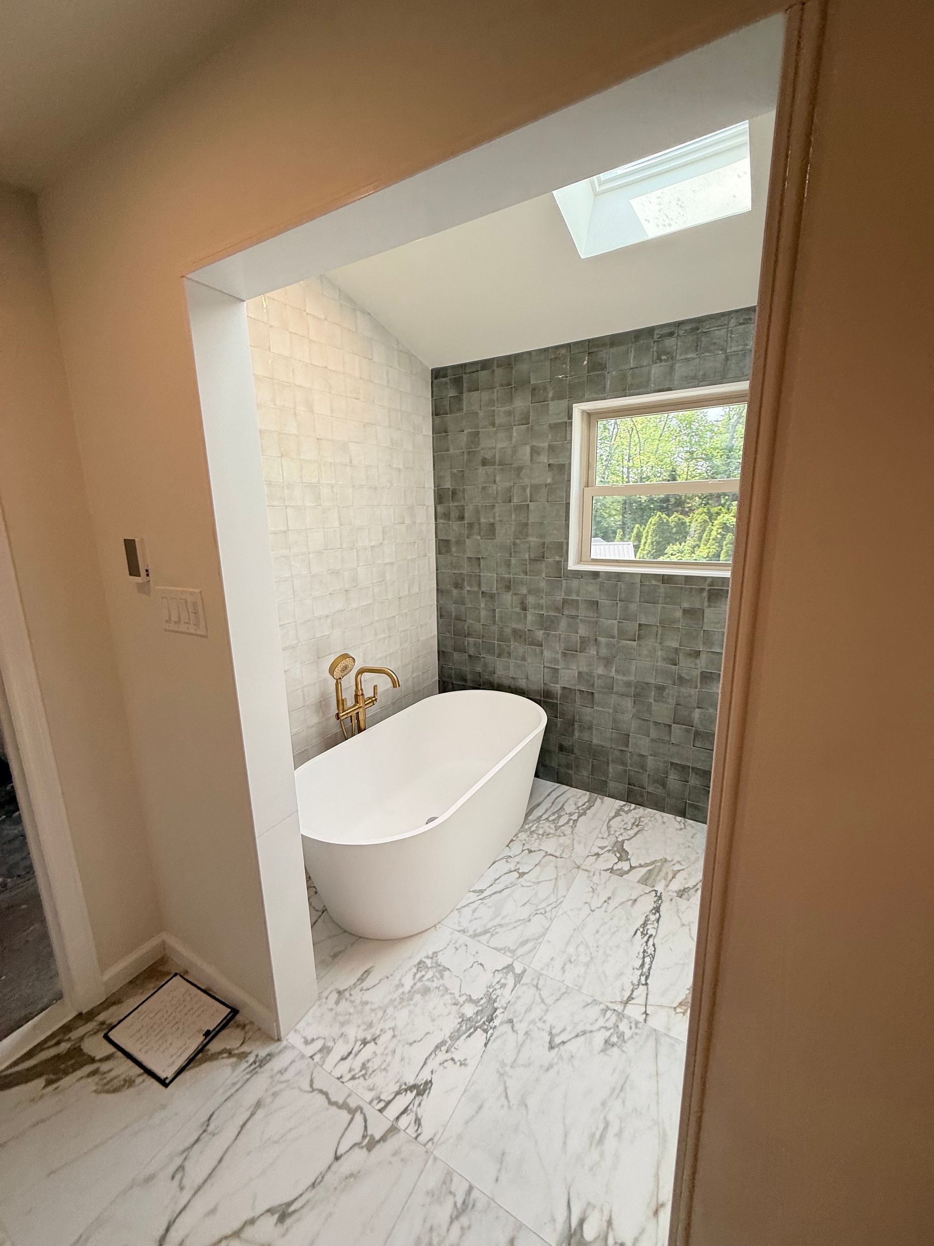 Bathroom with freestanding tub, marble tile floor, and accent tile wall; gold faucet; skylight.