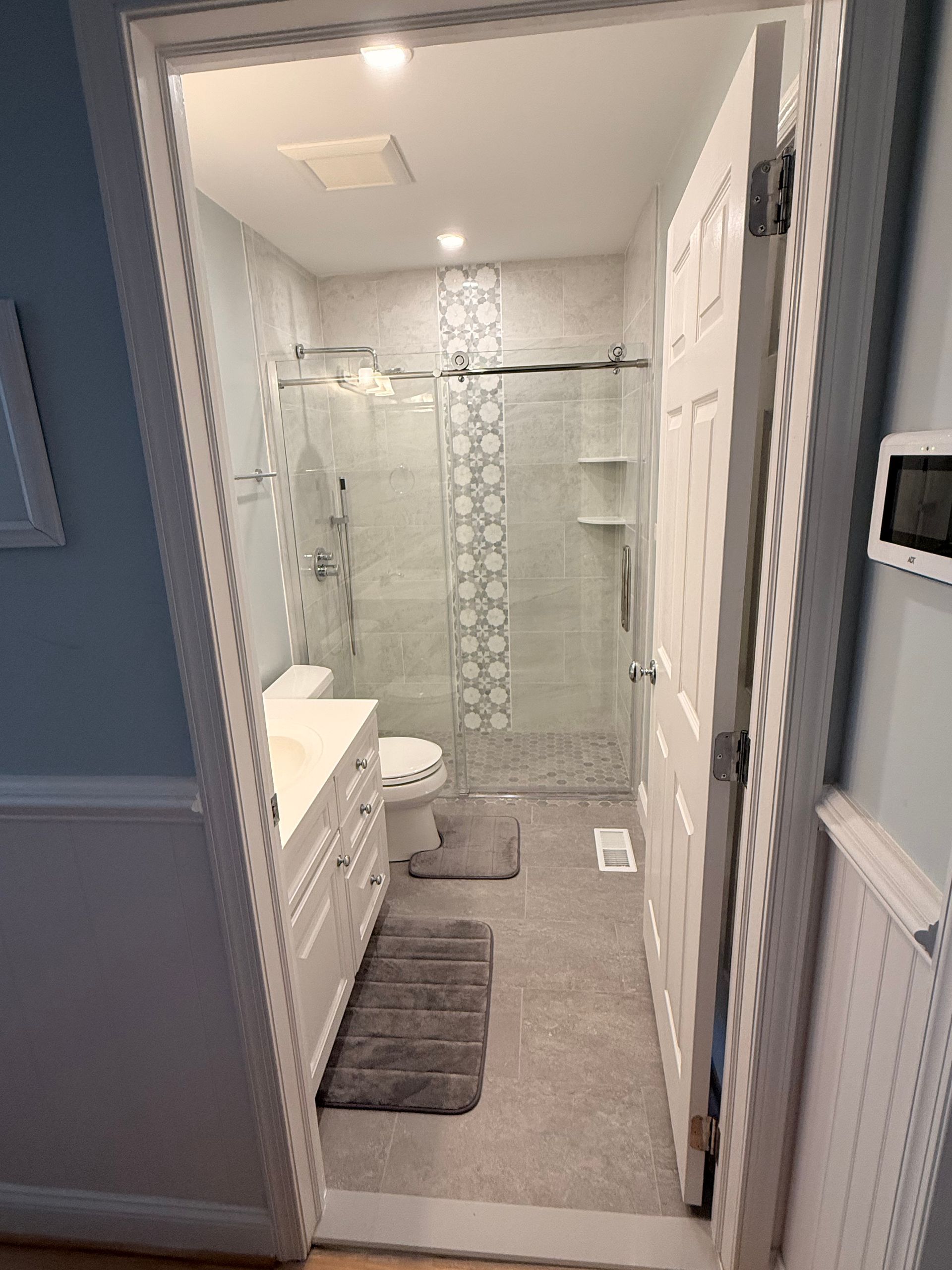 Bathroom with white vanity, gray tile, glass shower, and open door.