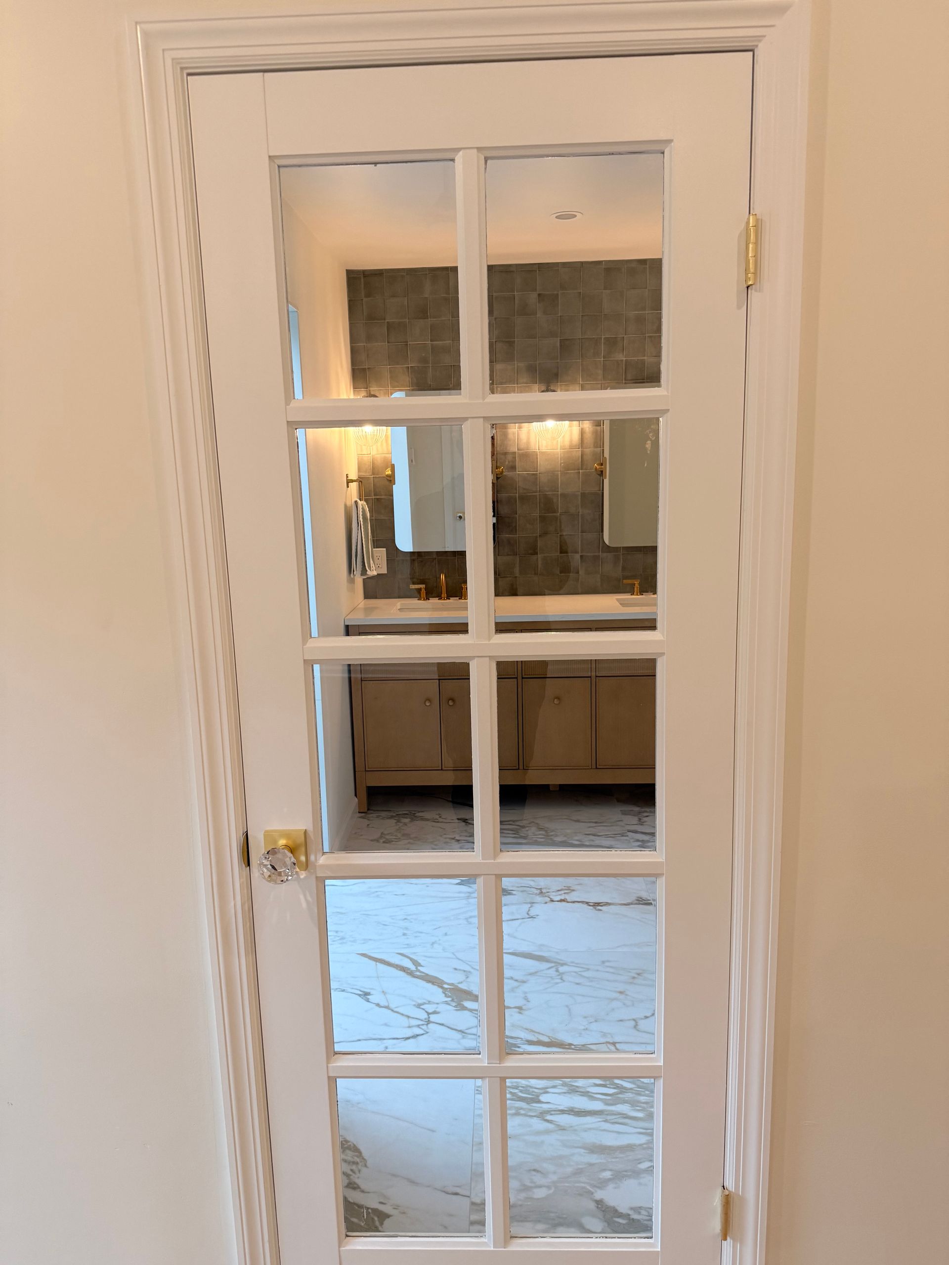 White French door with glass panels; view into a bathroom with a sink, mirror, and cabinetry.