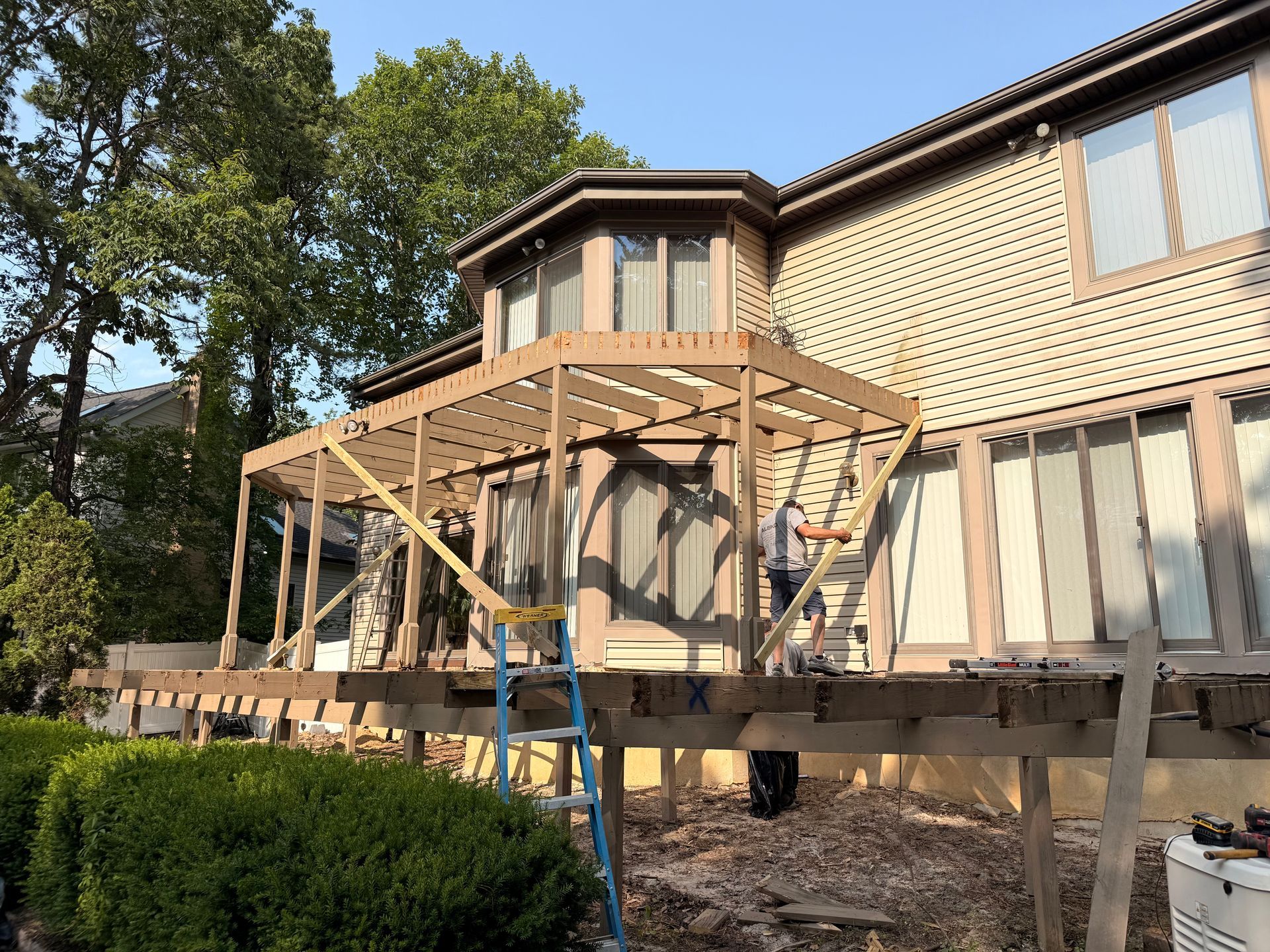 Construction of a deck cover on a house. Wooden frame, man working on ladder, outdoors.