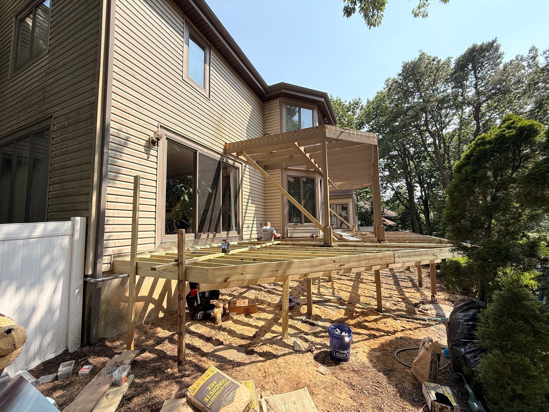 Deck construction with wood framing near a house, on a sunny day.