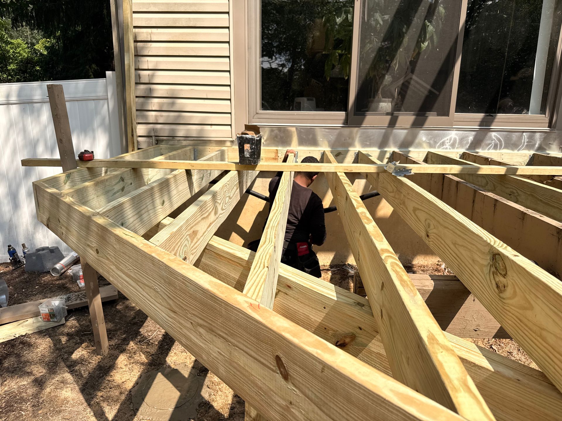 Deck construction: Wooden frame being built next to a building with a window. Person works within the frame.
