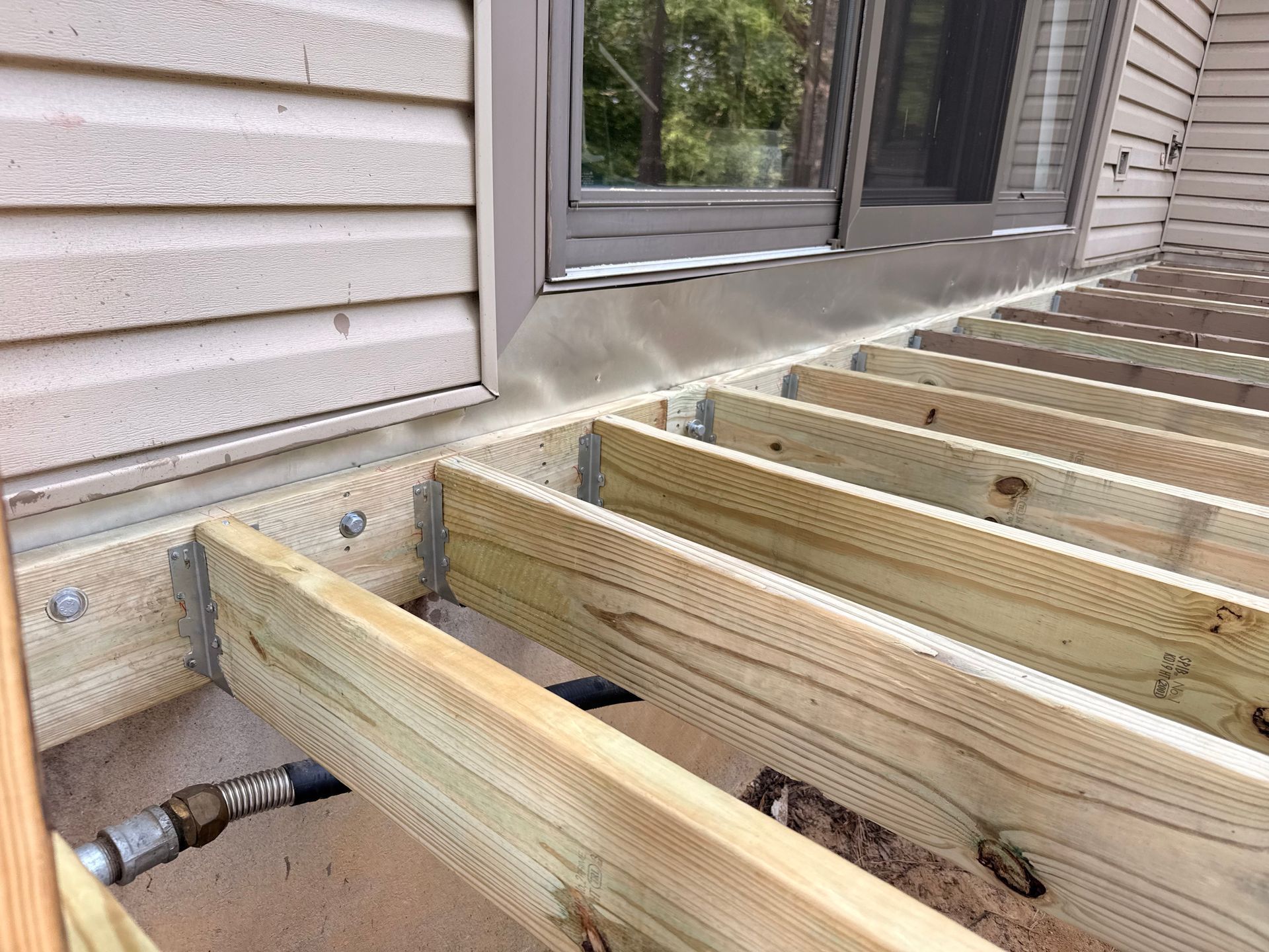 Deck under construction with wooden beams and a water pipe near a wall.