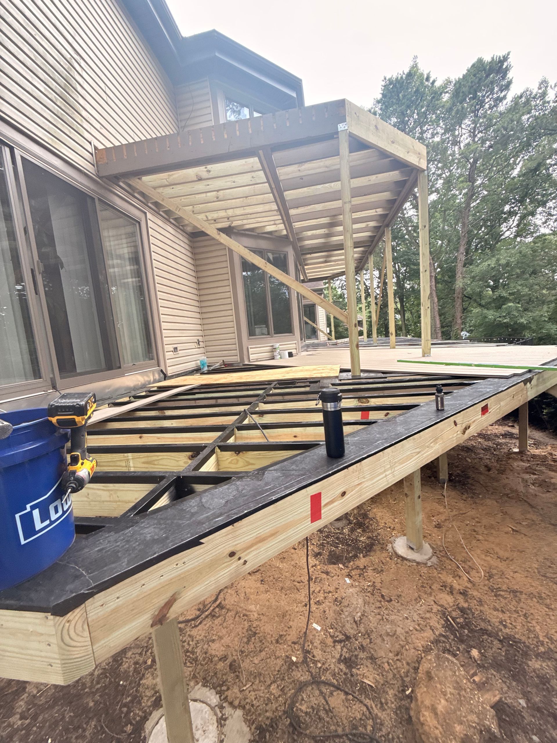 Deck construction in progress; wooden frame with a covered pergola attached to a house.