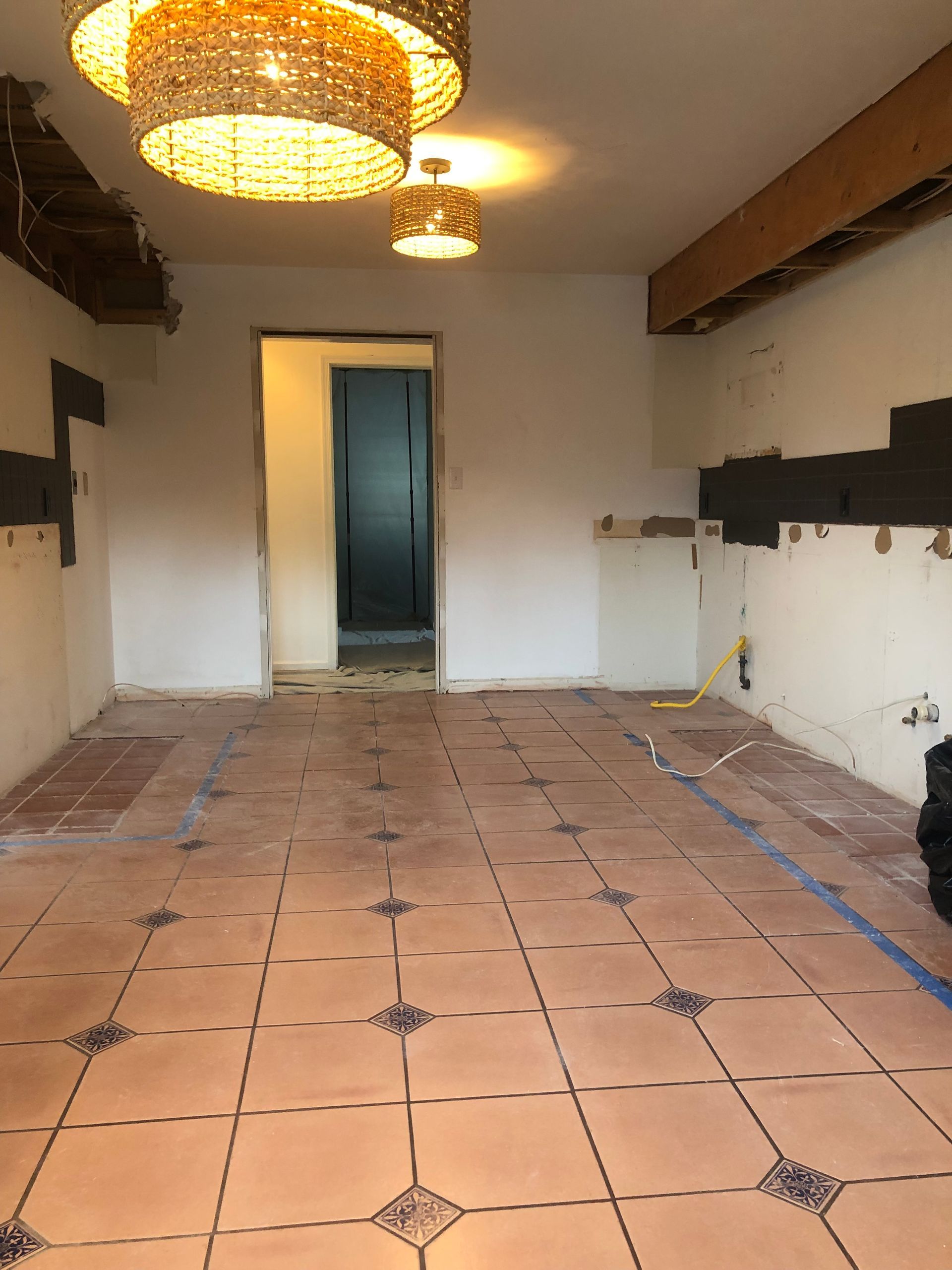 Room under renovation with terracotta tile flooring, exposed walls, and pendant lights.