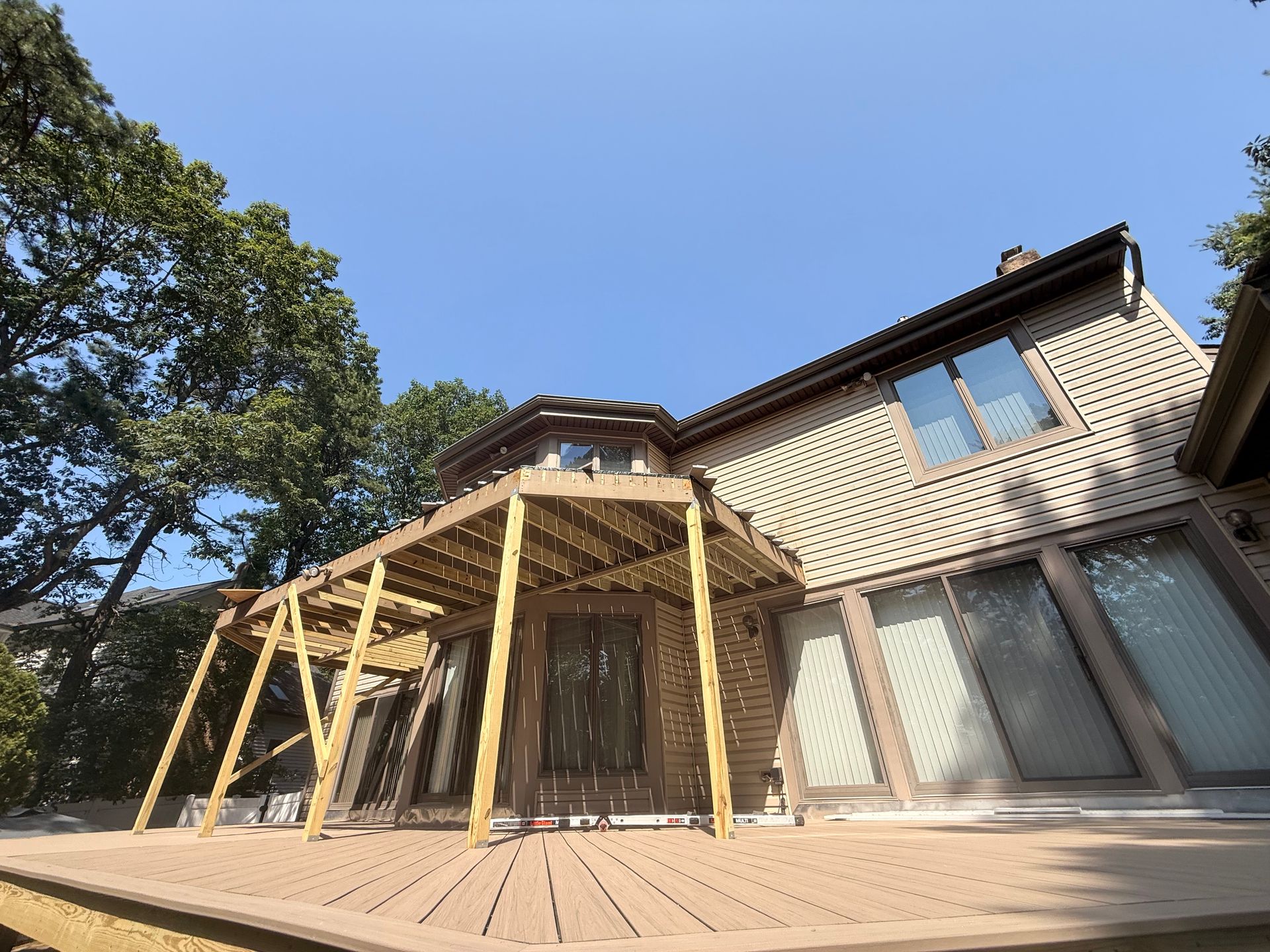Wooden deck and pergola attached to a two-story brick house on a sunny day.