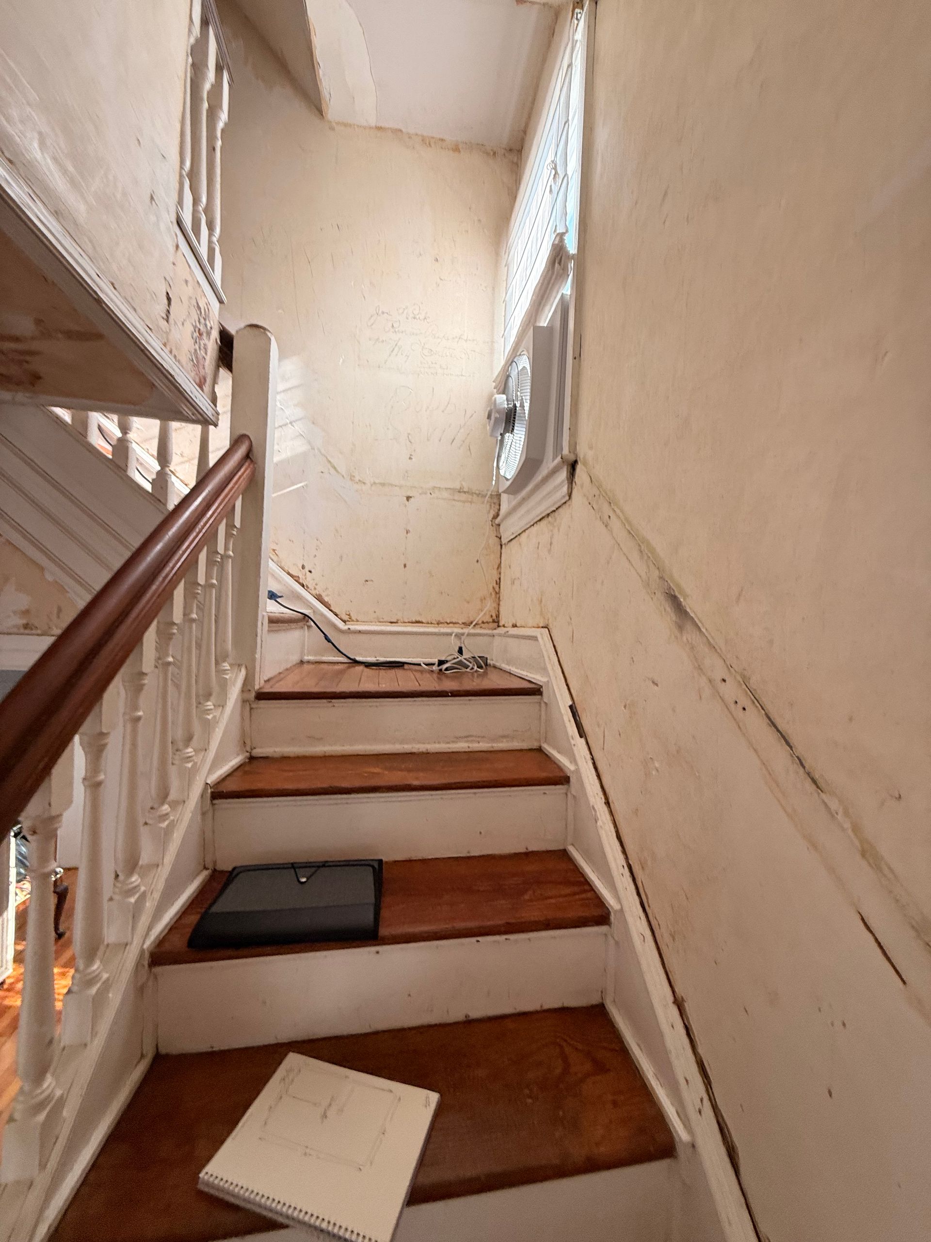 Wooden staircase with white banister, leading up to a landing with a window. Notebook on bottom step.