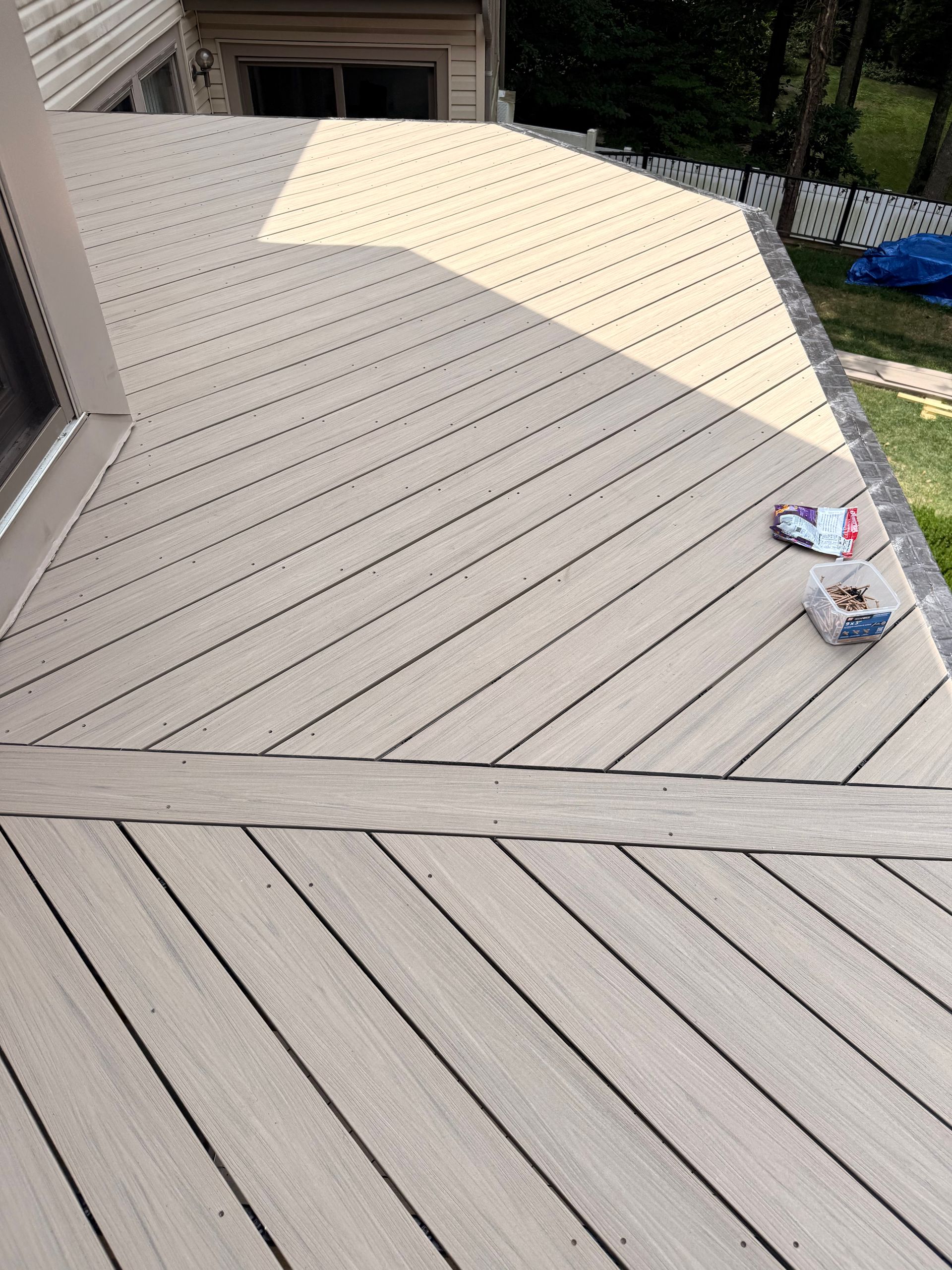 Angled composite deck boards, sunlight casting shadows, with debris.