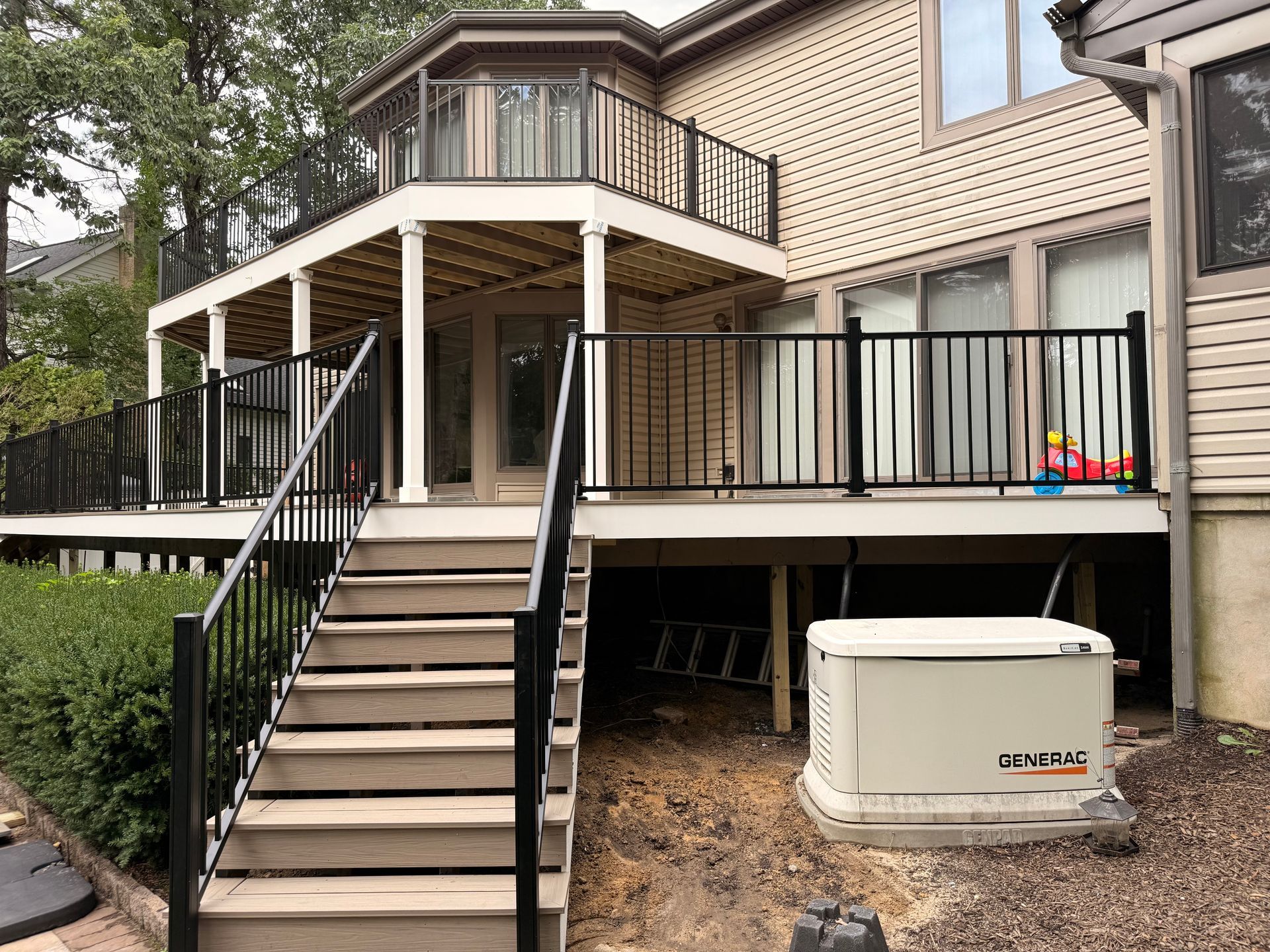 Multi-level deck with black railing and stairs leading to a house. A Generac generator sits below the deck.