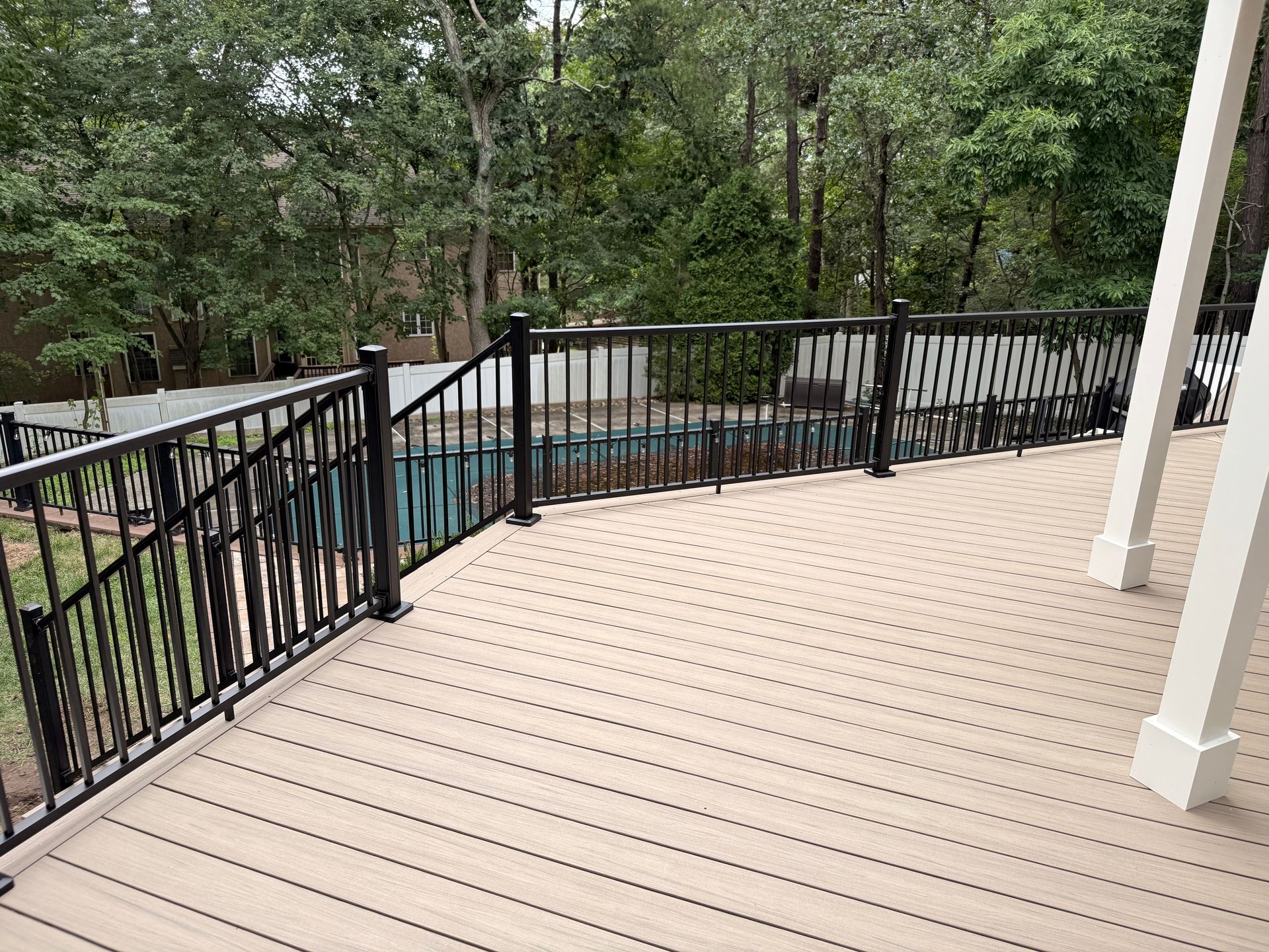 Deck with black railing overlooking a pool, surrounded by trees.
