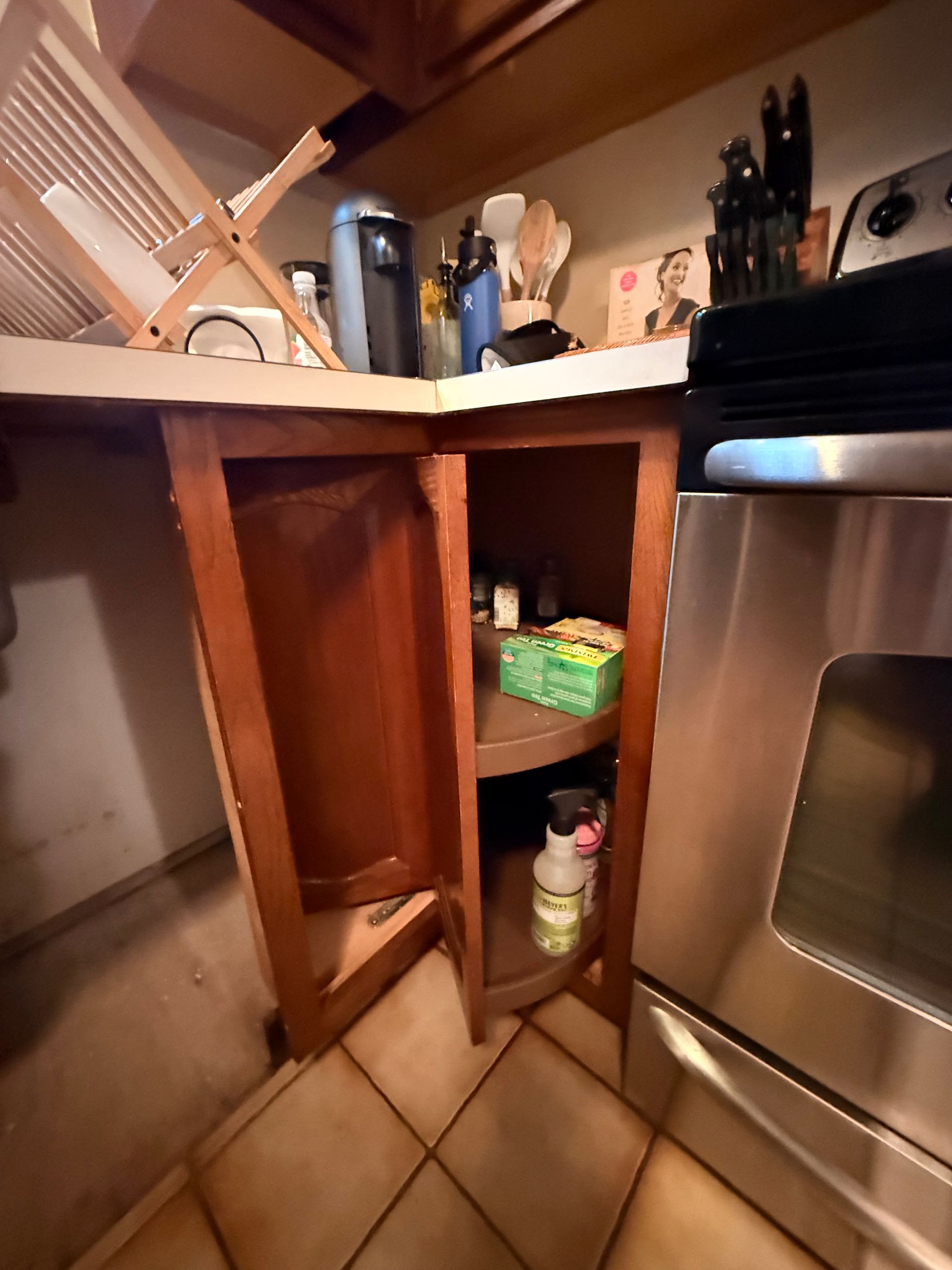 Kitchen cabinet with opened door, storing items; adjacent to a stainless steel stove.
