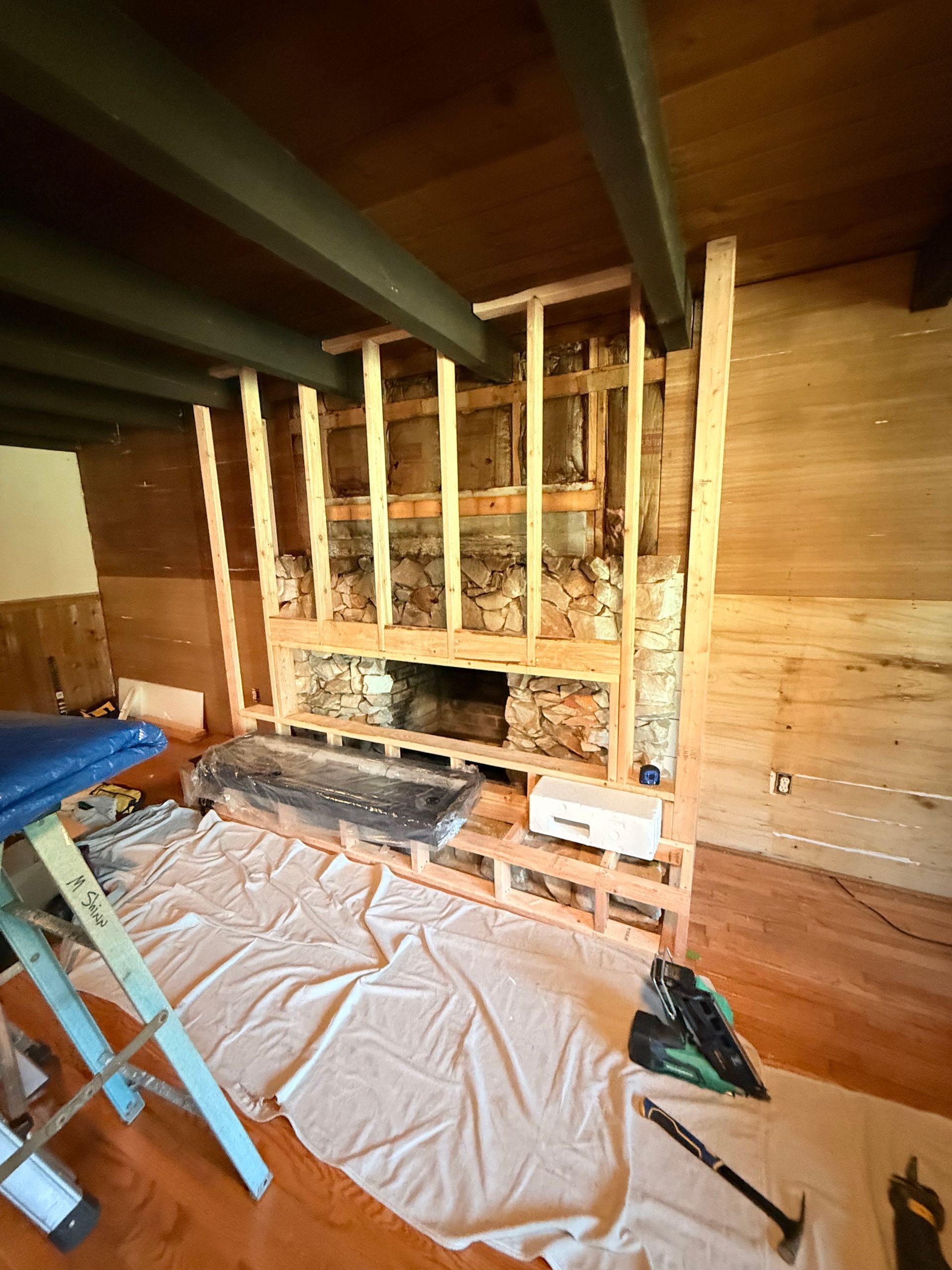 Construction framing around a fireplace. Wooden beams, brick hearth, and wall sheathing in a room under renovation.