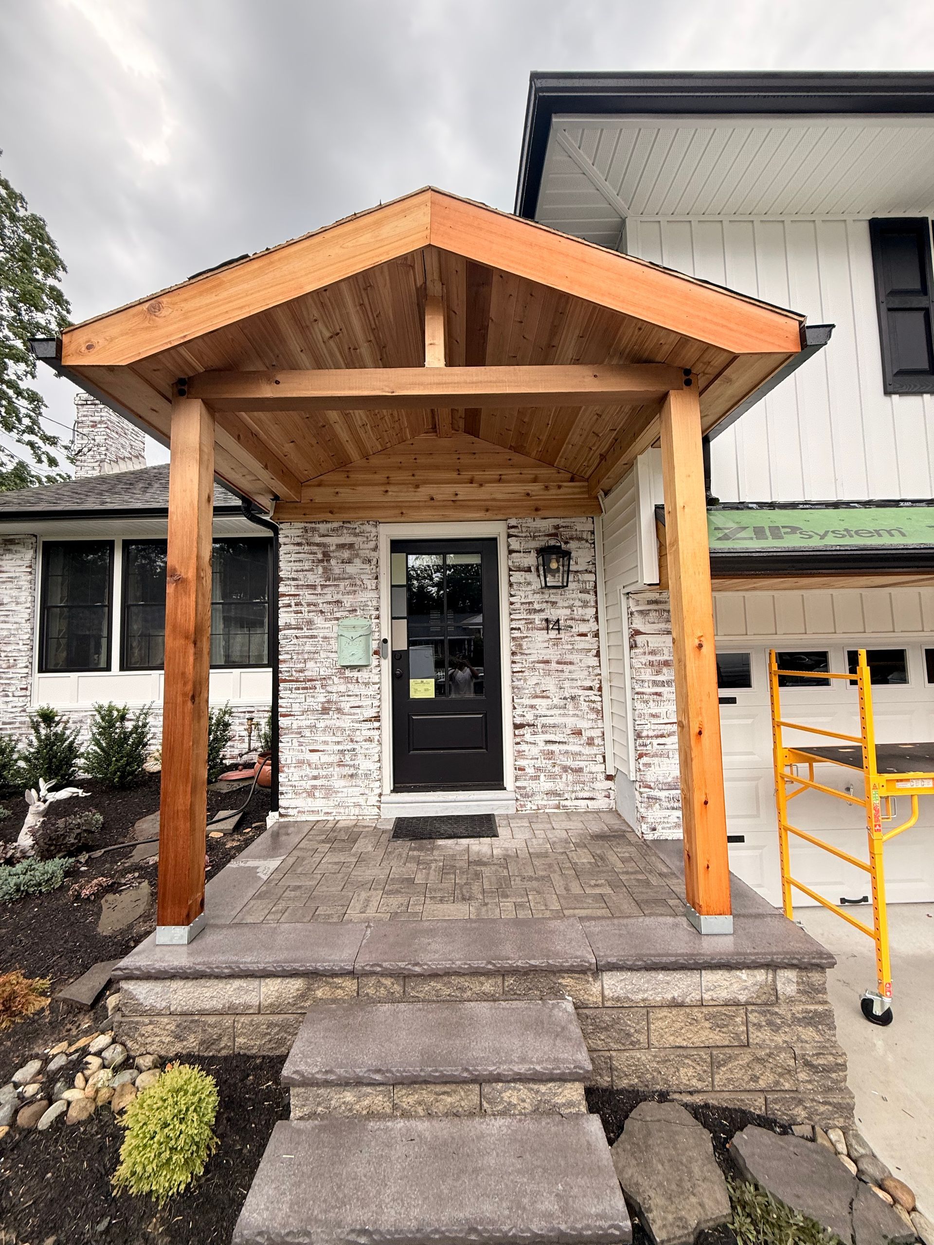 Wooden porch entry with brick facade, black door, and layered stone steps.