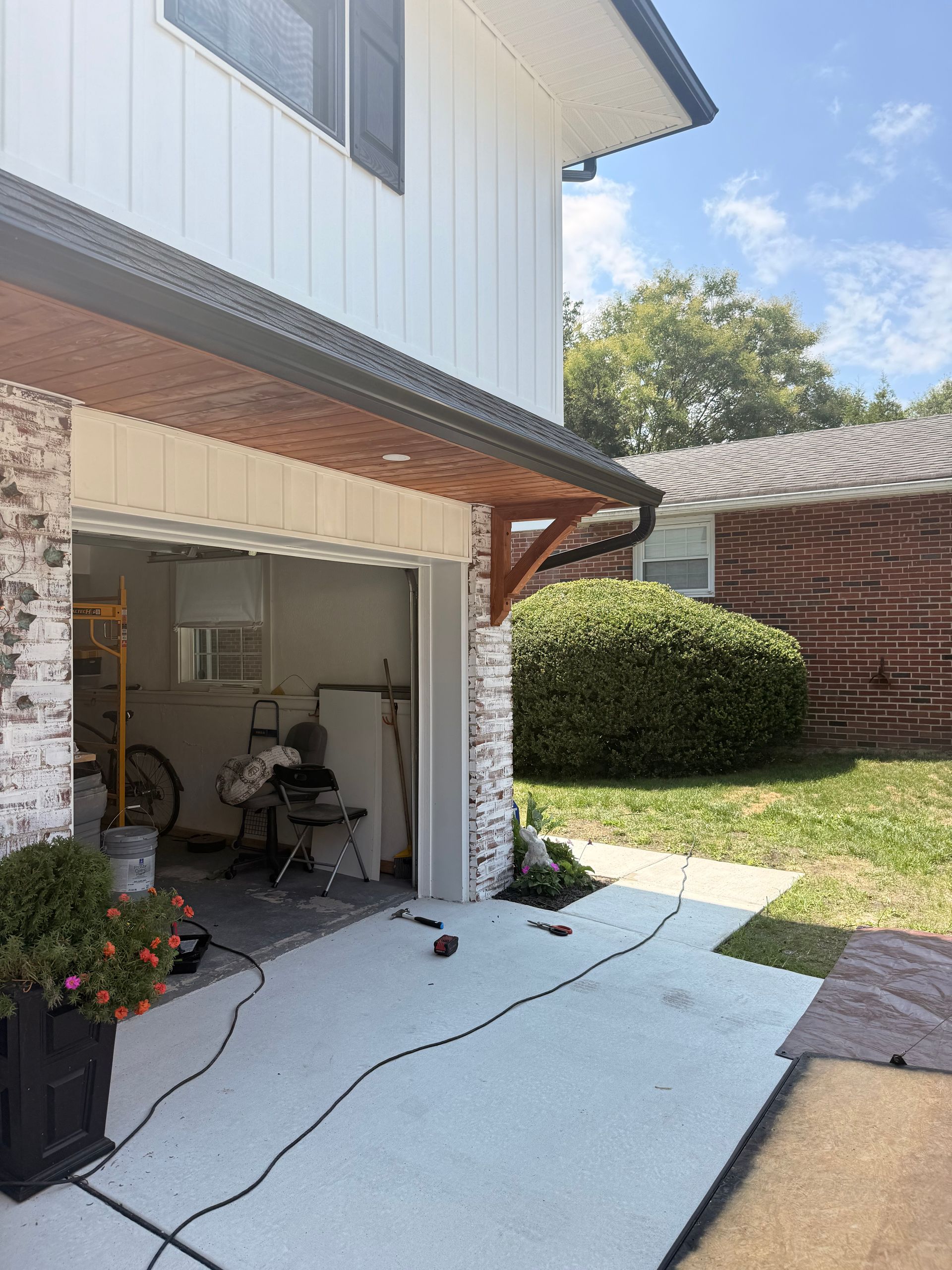 Garage exterior with white siding, brick, and brown trim. Open door, concrete, and green yard.