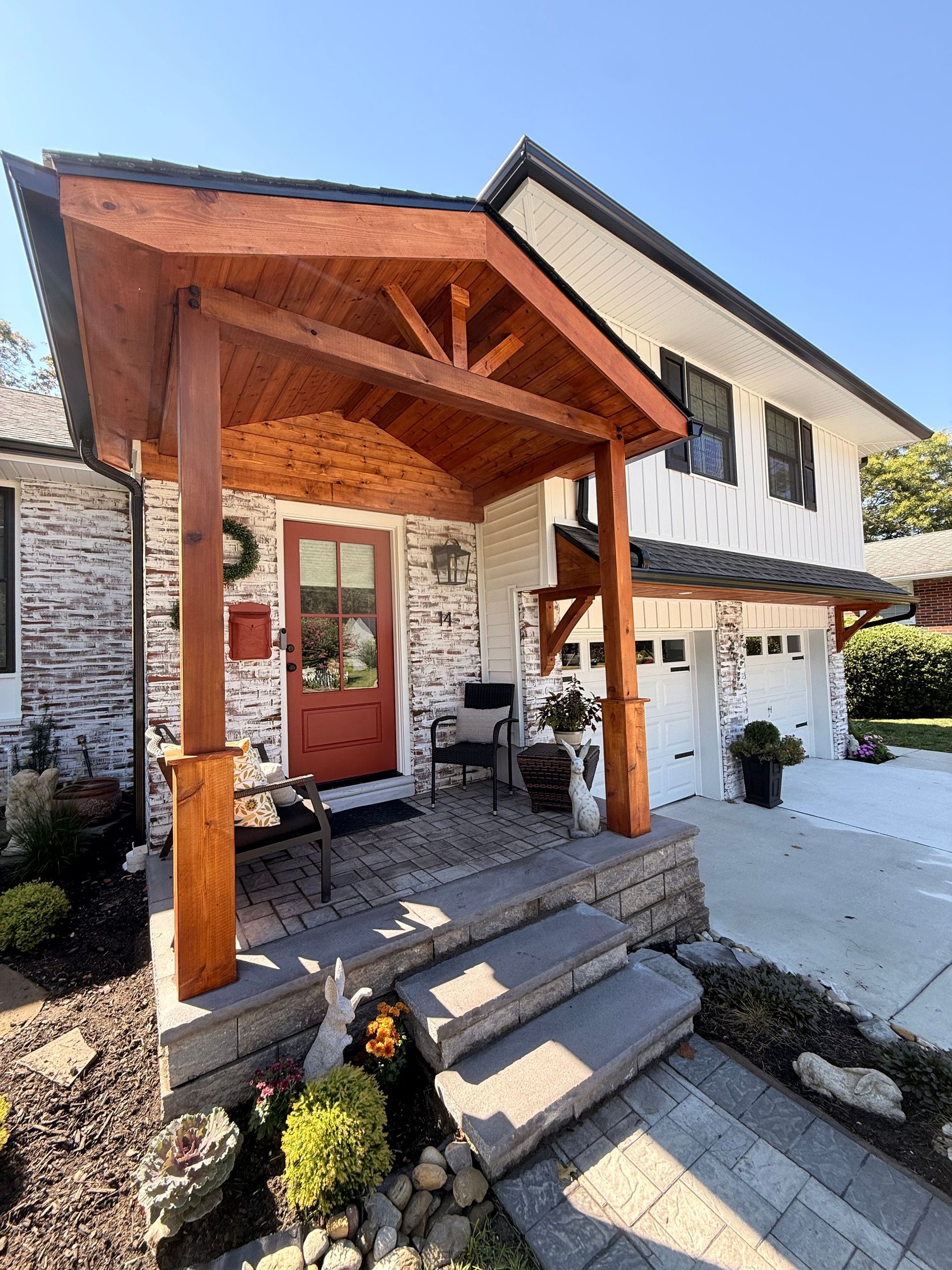 A house with a red door and a wooden porch. Brick facade, white siding, and a two-car garage.