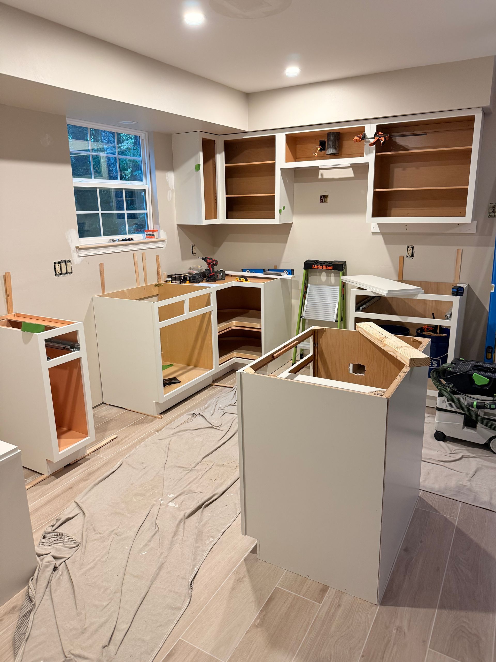 Kitchen undergoing renovation, cabinets partially installed, covering on the floor.
