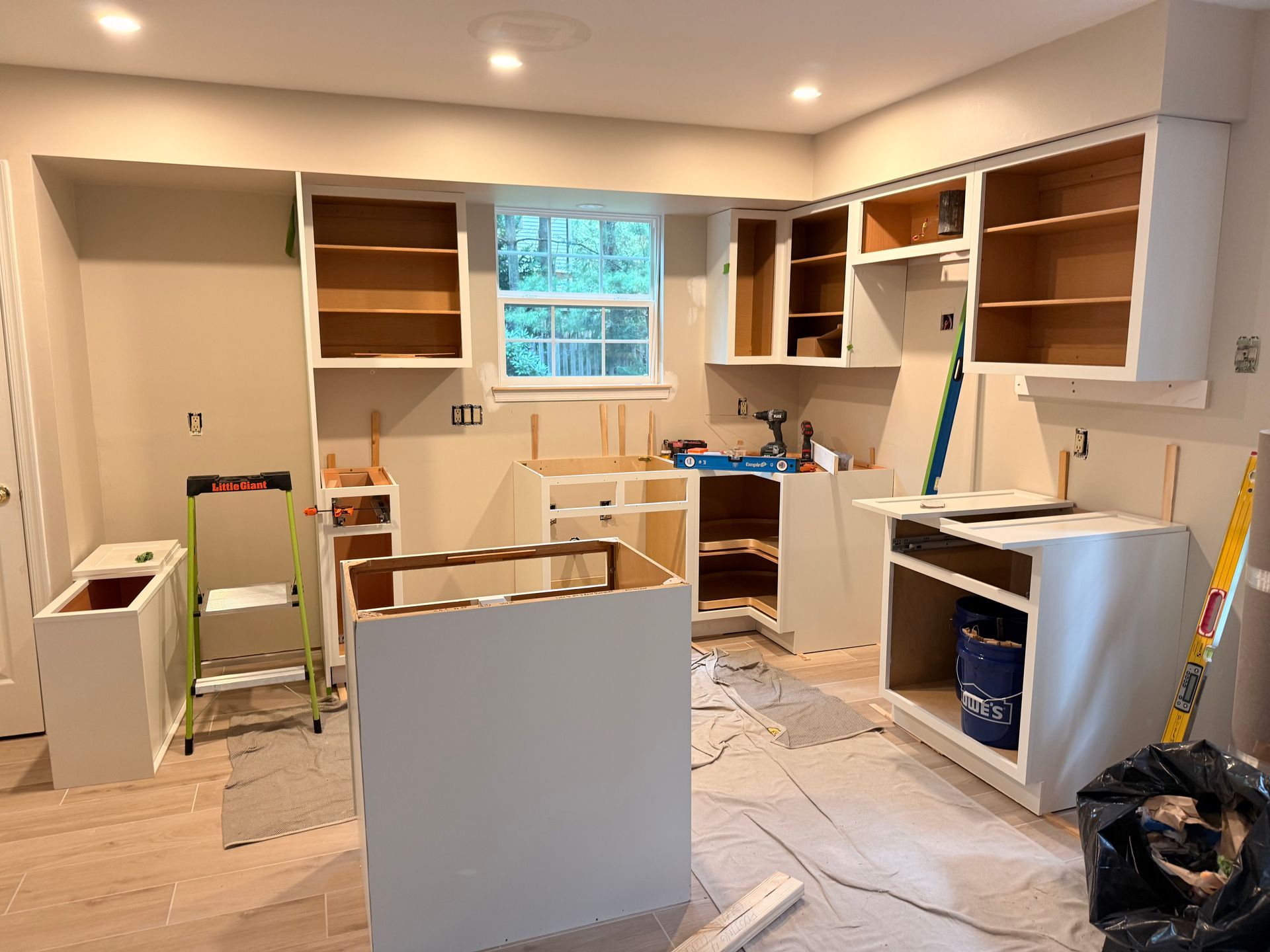 Kitchen under renovation; white cabinets installed, plywood shelving, and tools scattered.