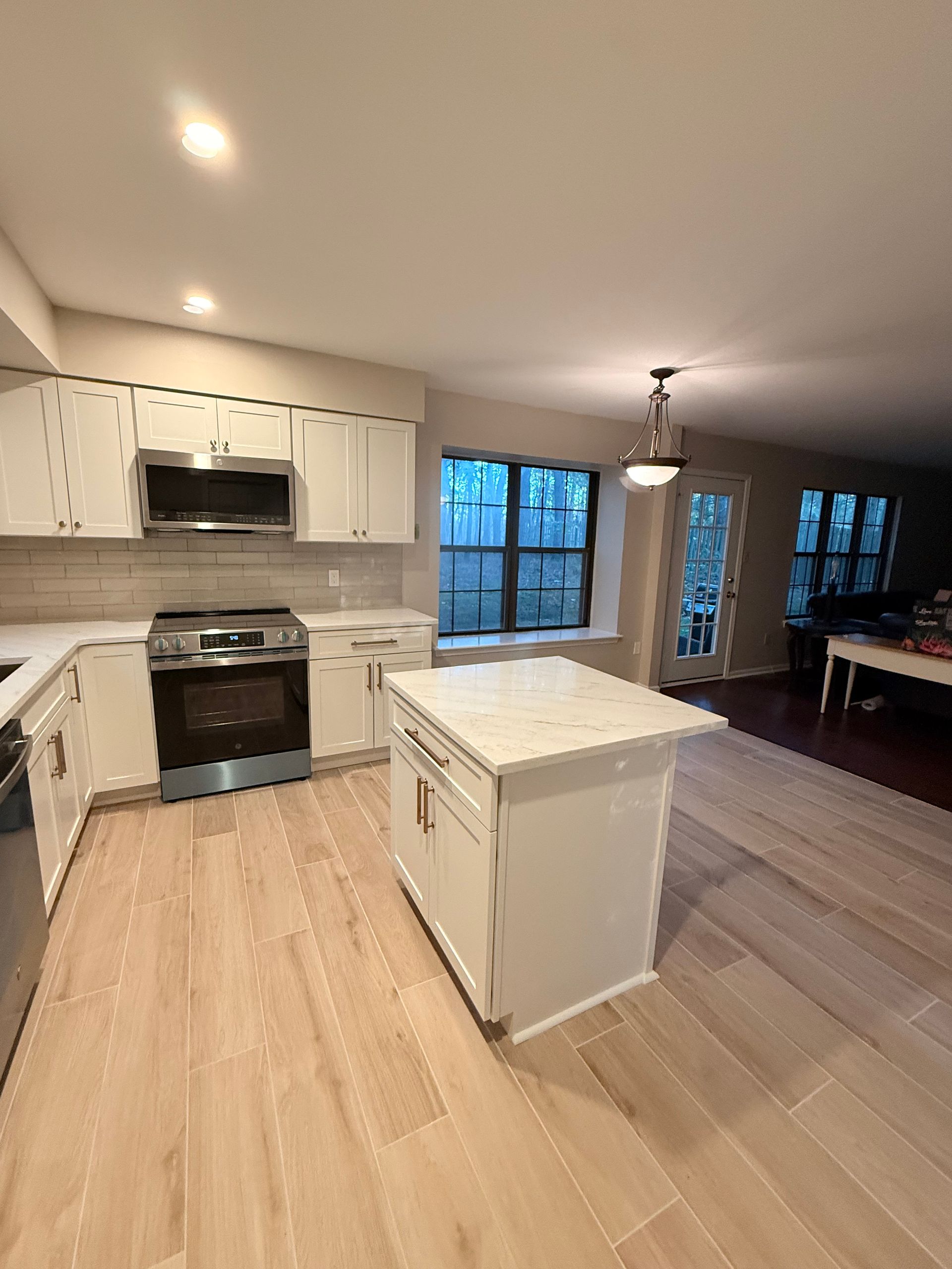 White kitchen with island, stainless steel appliances, and wood-look flooring.