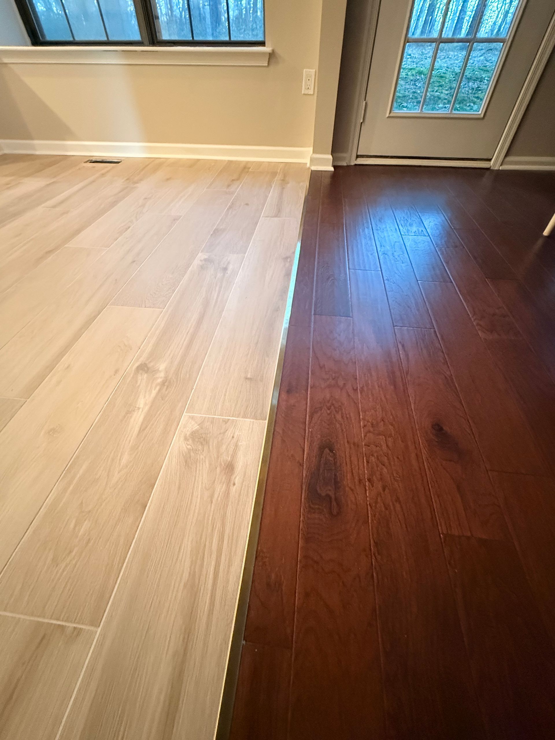 Light-colored tile floor transitions to dark-stained hardwood floor in a room, split down the middle.