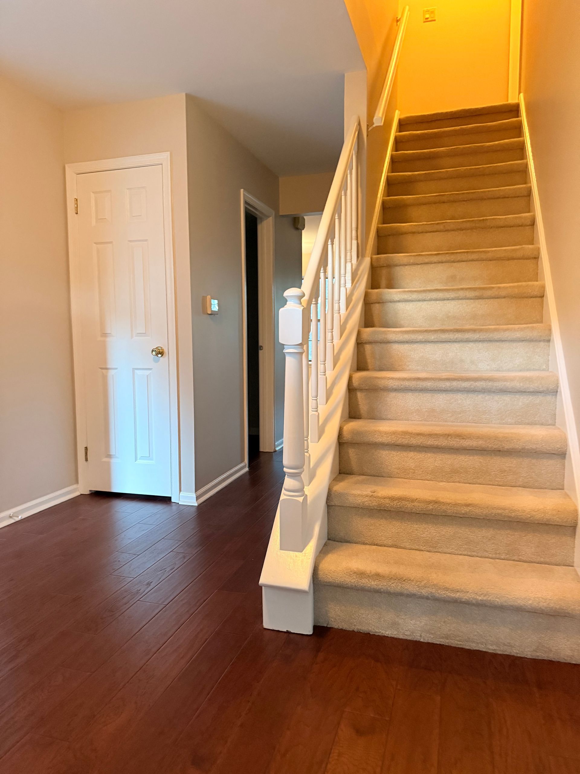 Interior view: Entryway with staircase and closed door. Wood floors, carpeted stairs, and neutral walls.
