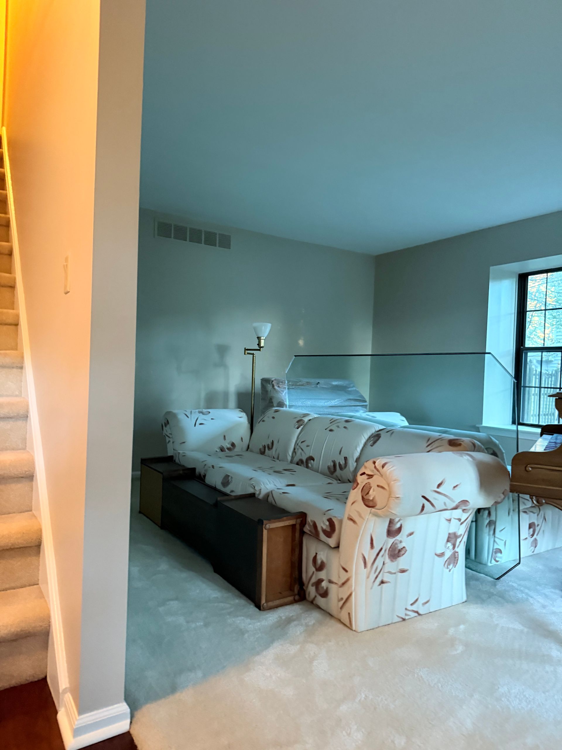 Beige living room with sofa and stairs to the left. Bright light, white carpet.