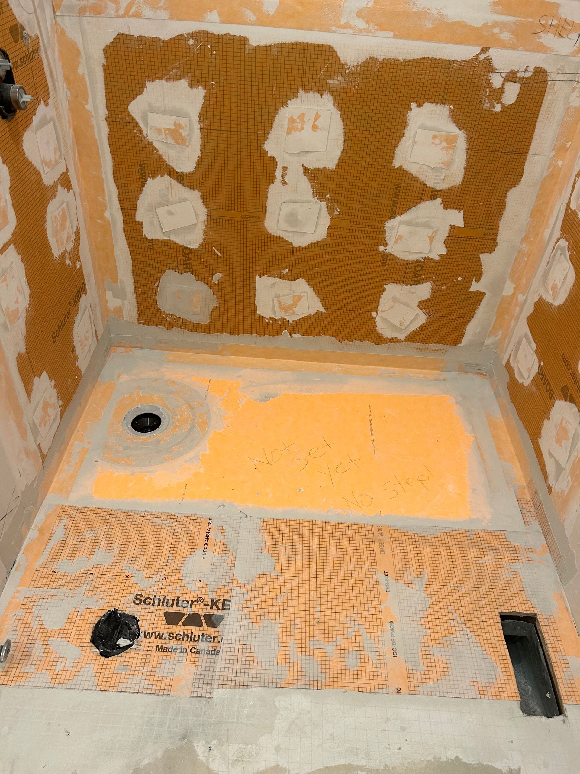 Shower stall under construction, orange waterproofing membrane on walls and floor. Black holes for plumbing.