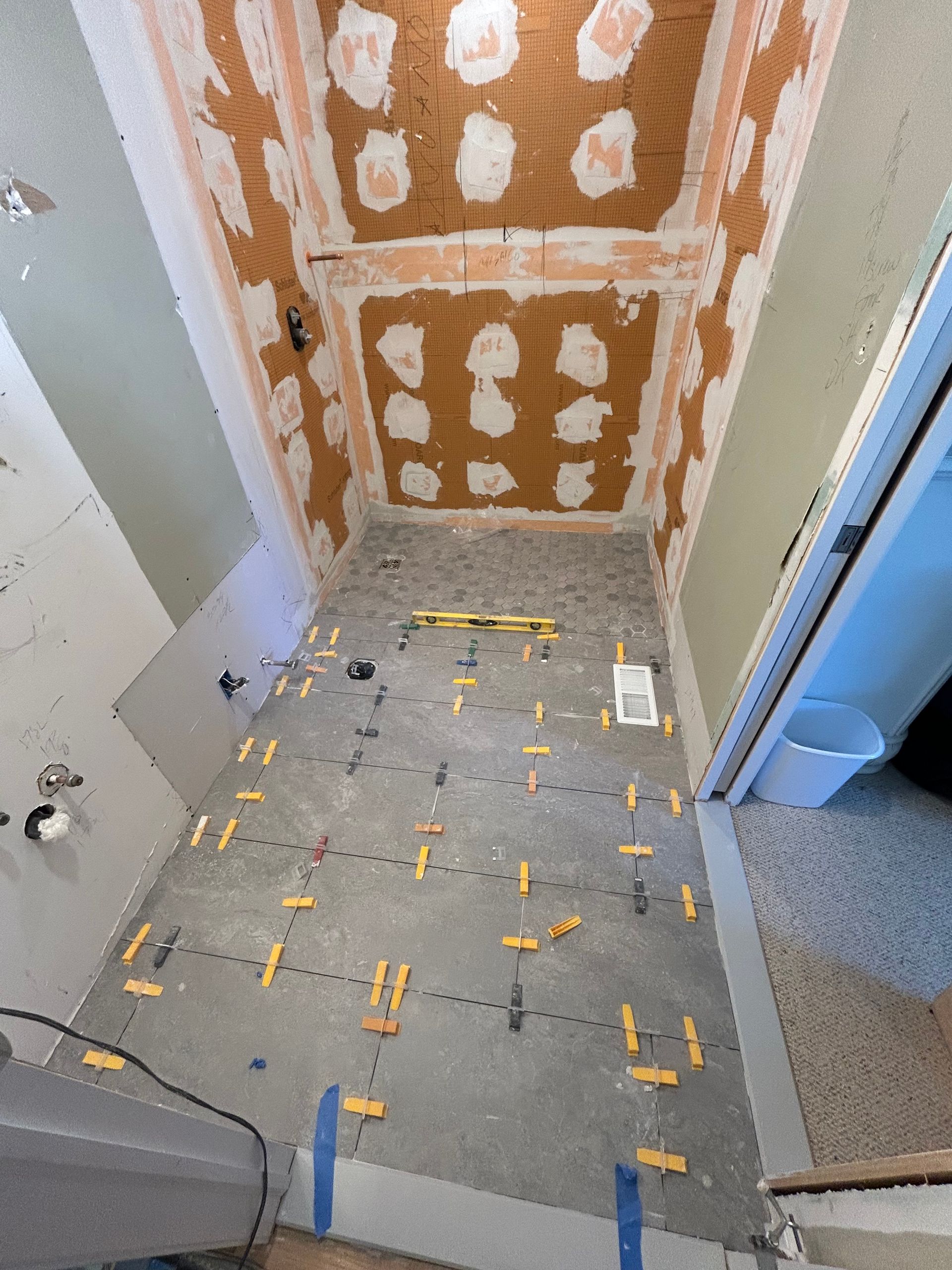 Bathroom renovation in progress; floor tiles laid with spacers. Walls have exposed plaster.