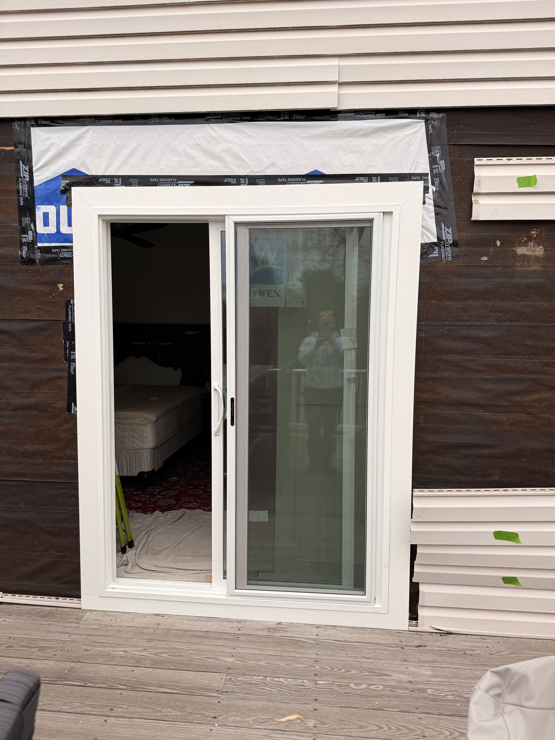 Sliding glass door, white frame, installed in a wall.  Exterior of the structure has brown siding and black paper.