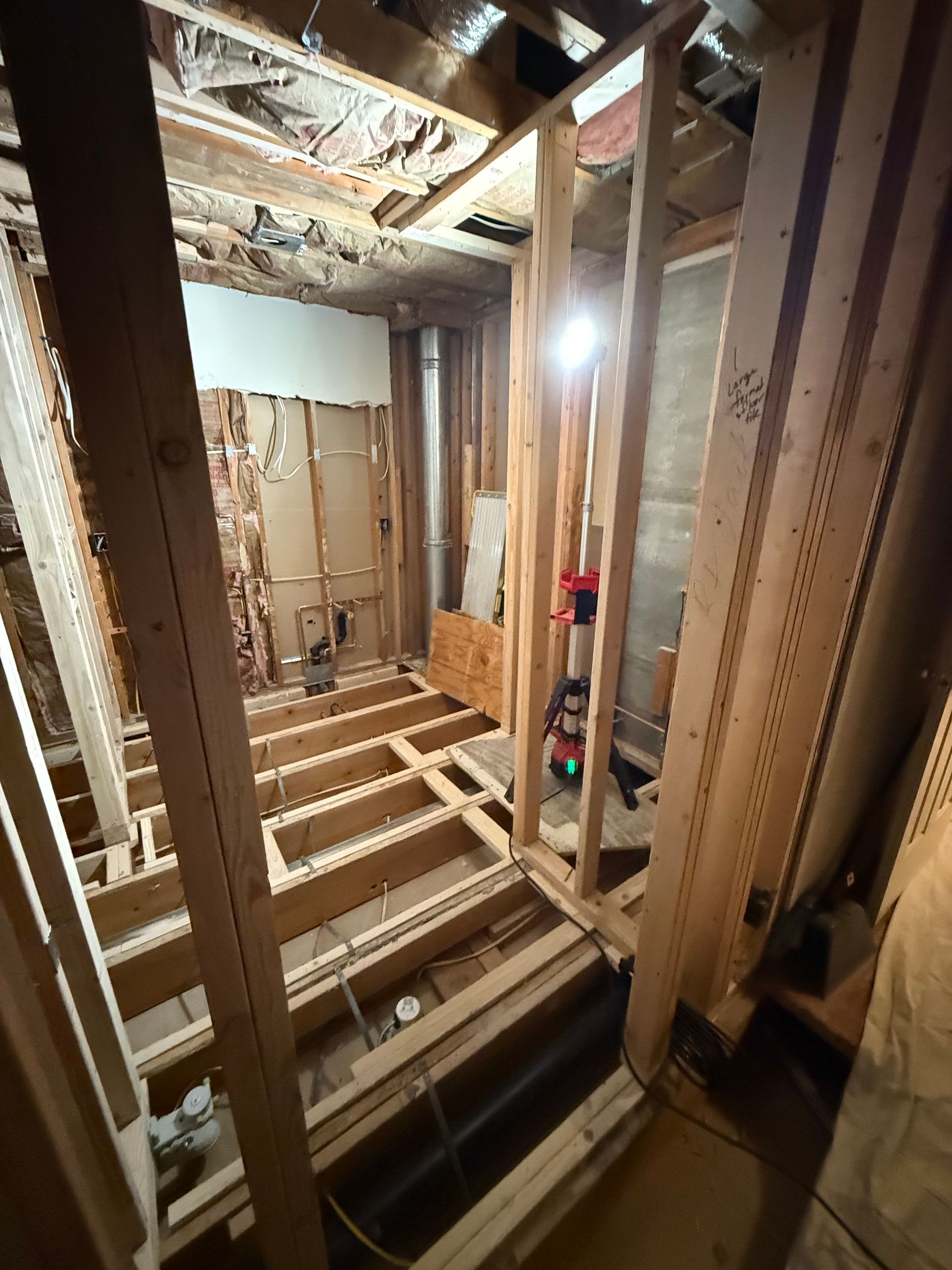 Bathroom renovation in progress, interior view. Wooden studs and floor joists exposed, framing the future space.