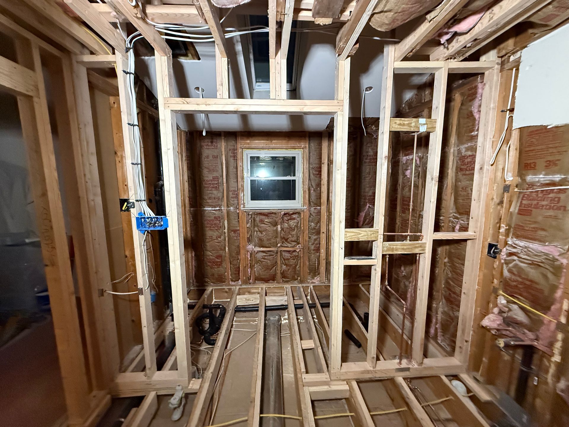 Interior framing of a room under construction with exposed studs, insulation, and wiring.