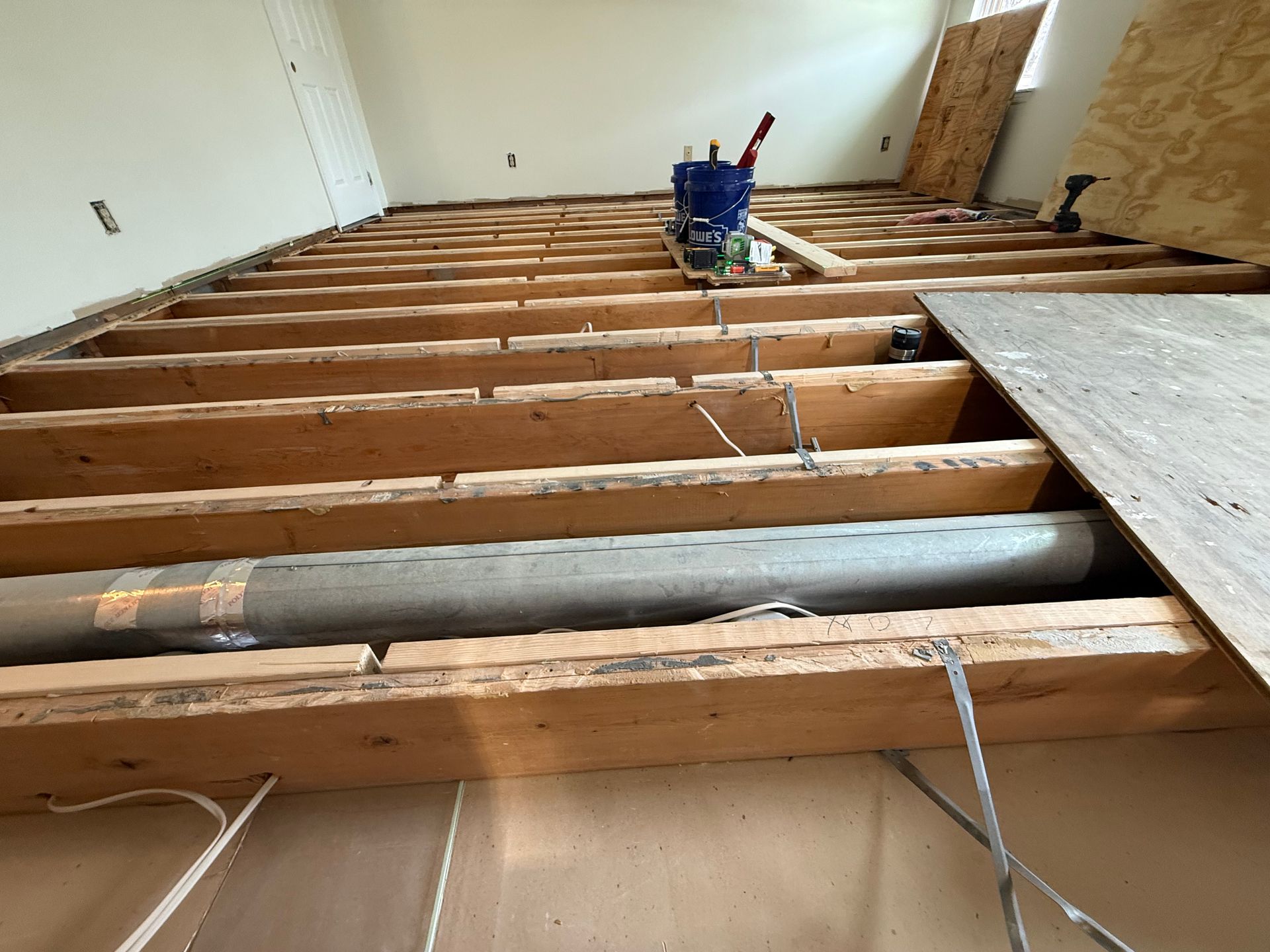 Exposed floor joists during construction, with ductwork, tools, and partial subflooring visible.