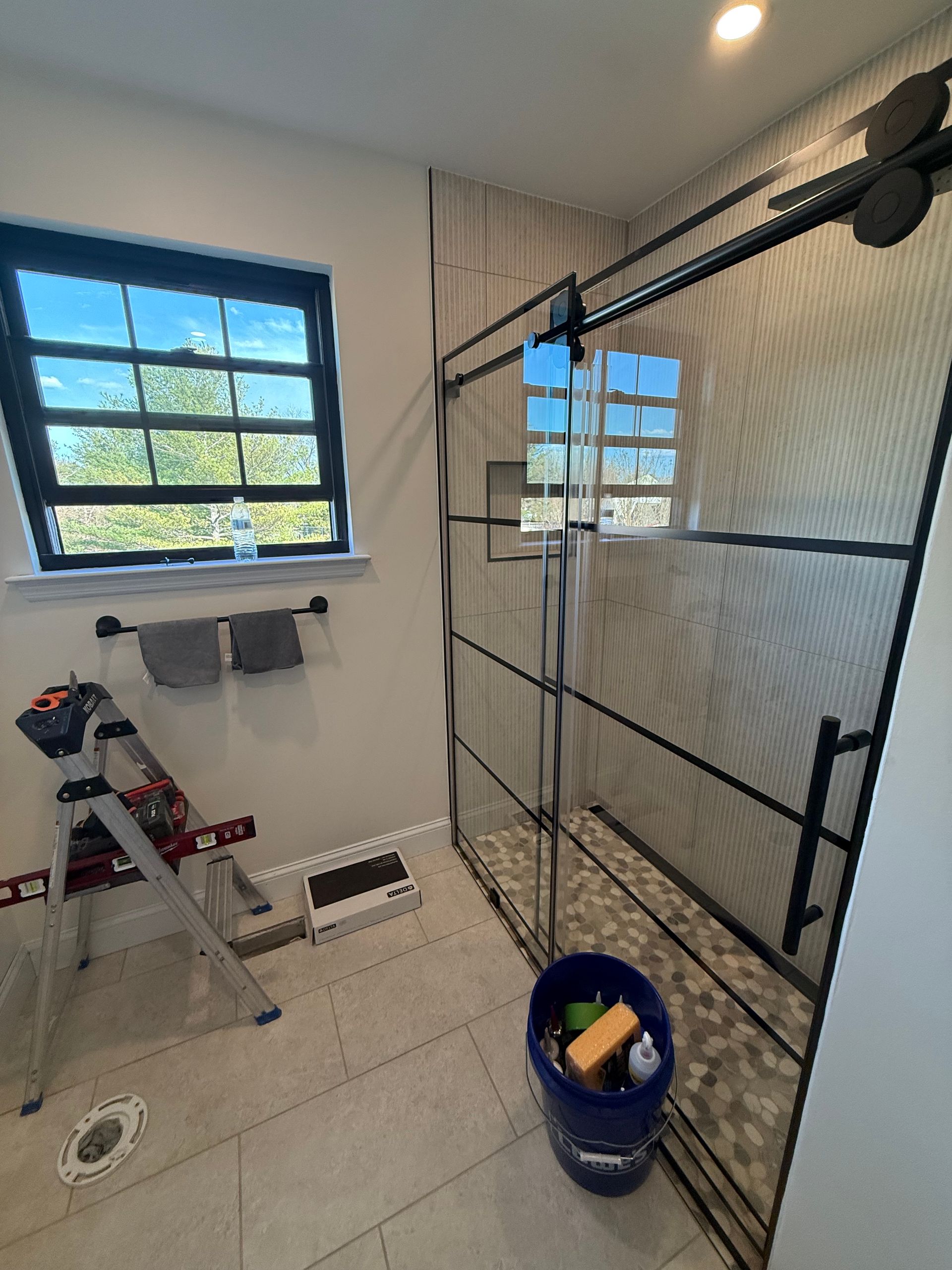 Bathroom with shower and window, unfinished with tools and ladder visible.
