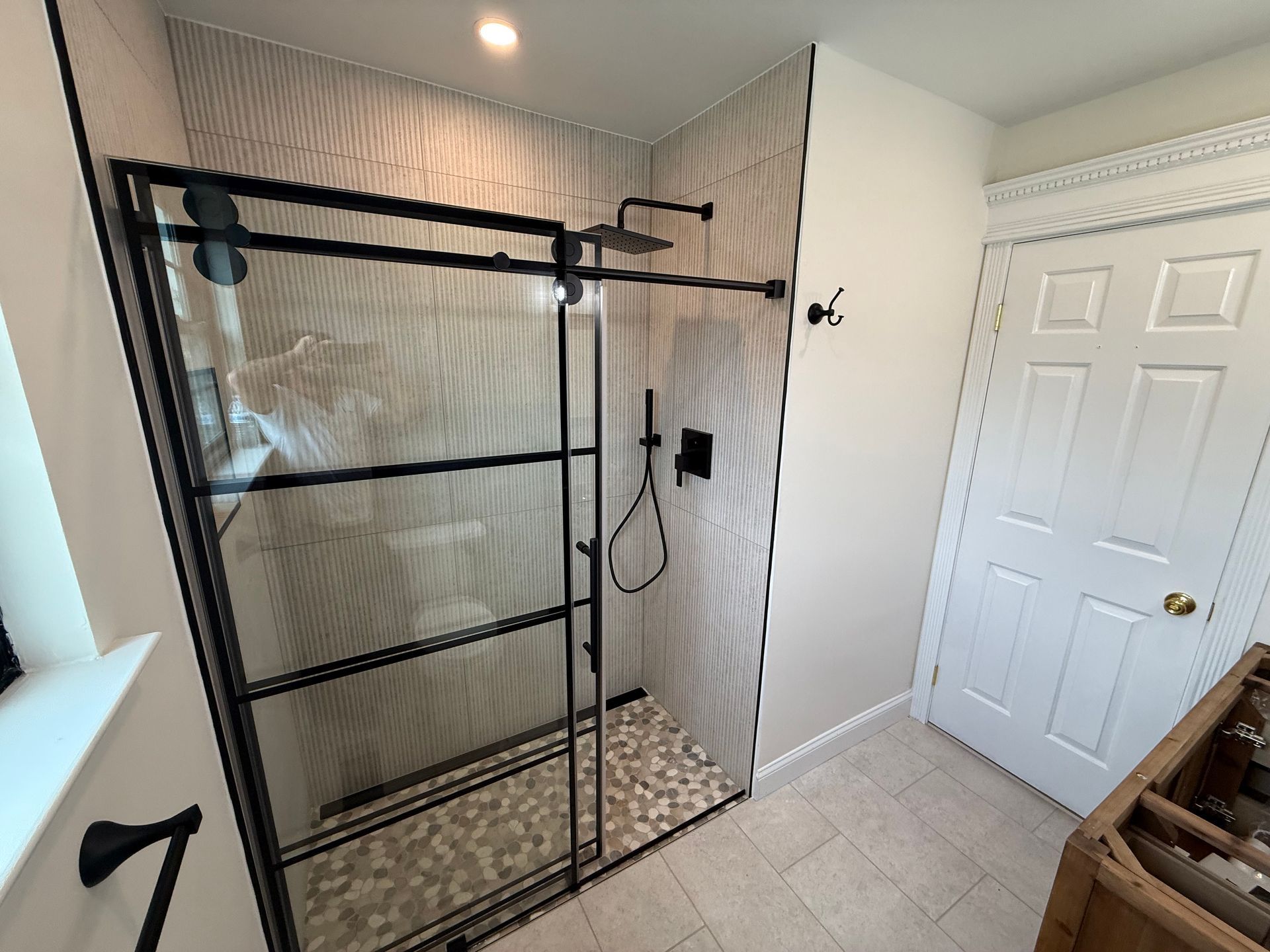 Modern shower with black-framed glass enclosure, stone tile floor, and light-colored walls.