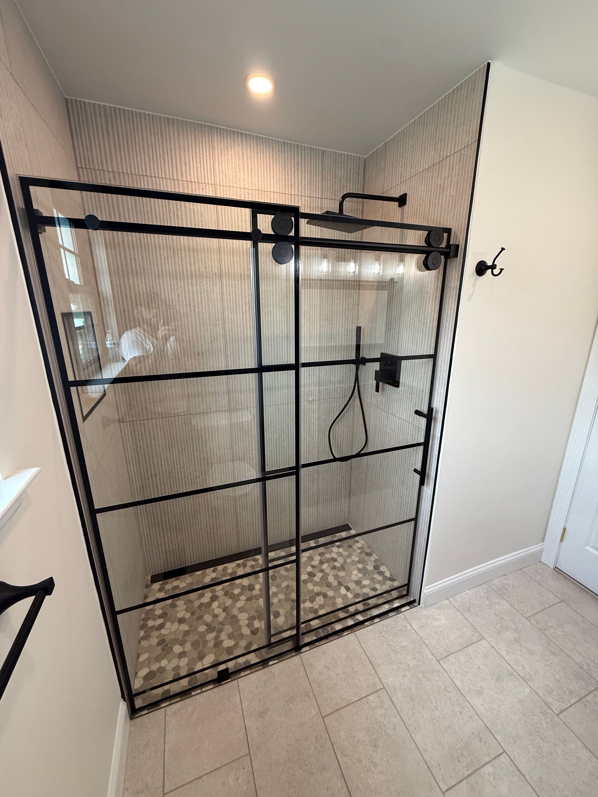 Glass shower enclosure with black metal frame and pebble tile floor.