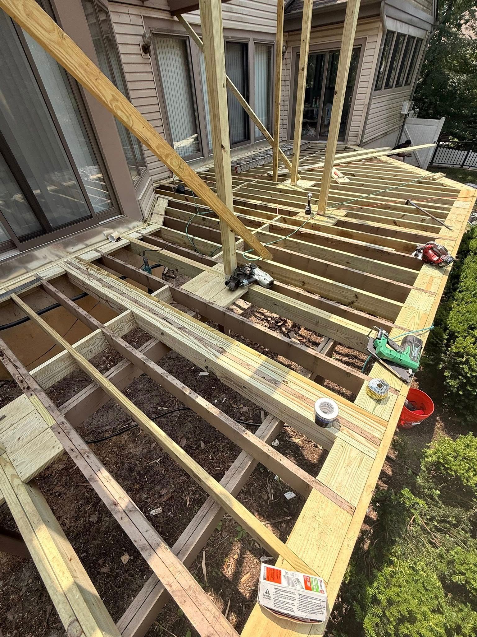 Deck under construction, with wooden beams and support posts visible. House exterior in background.