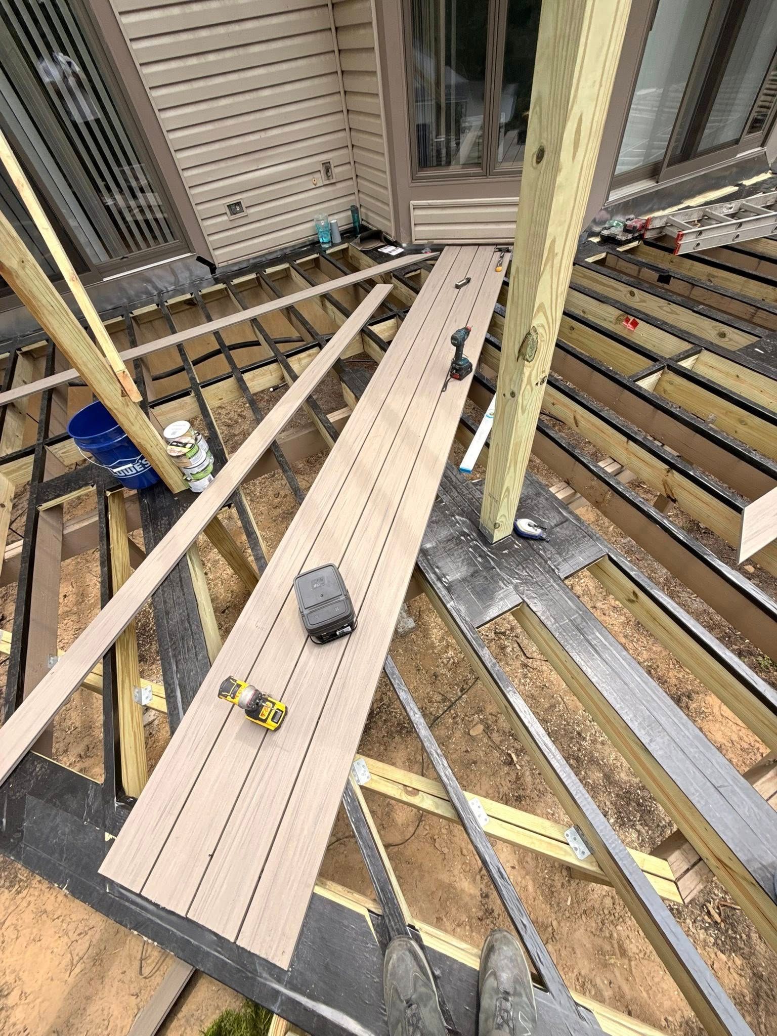 Deck construction, close-up view; composite boards and supports with tools on unfinished surface near house.
